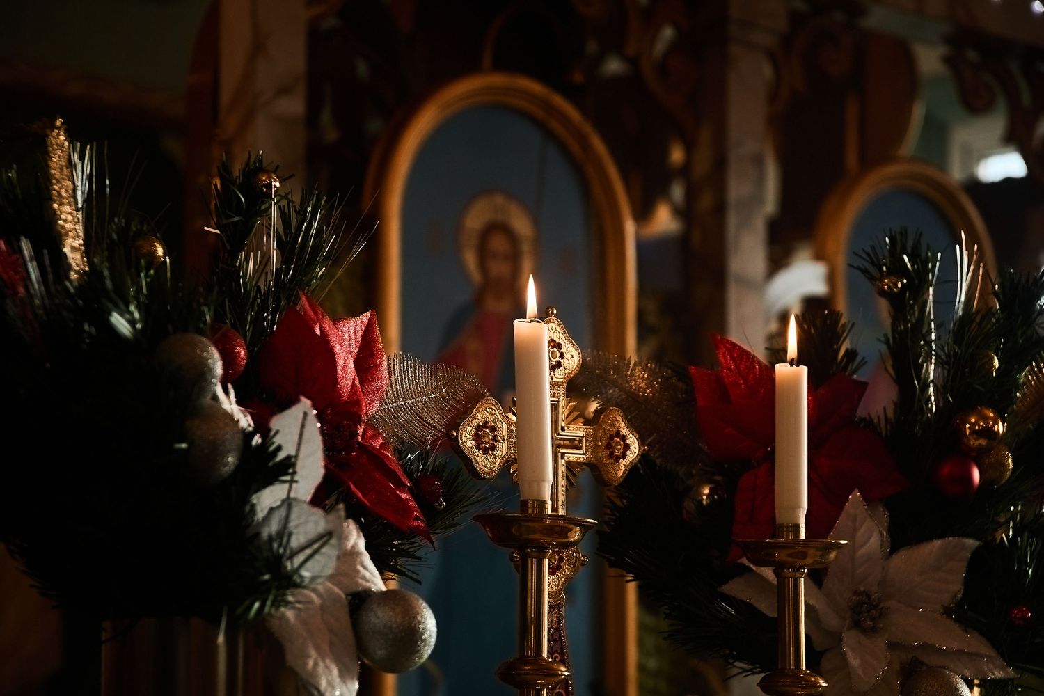 Lit candles and holiday decorations in front of religious icons create a reverent atmosphere.