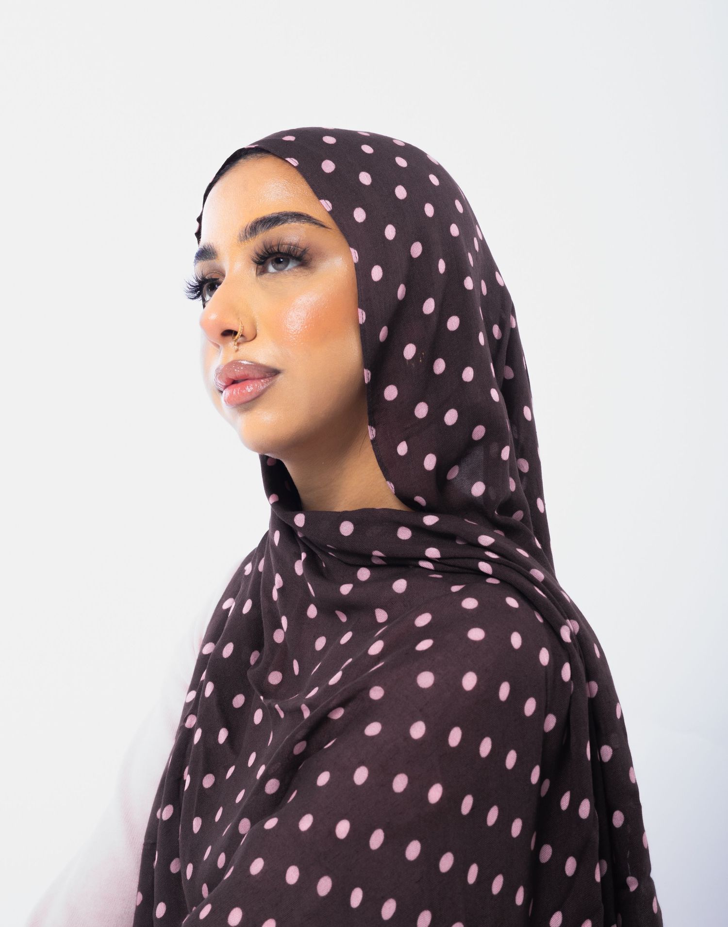 Woman wearing a dark brown polka dot hijab with pink spots, posing against a white background.