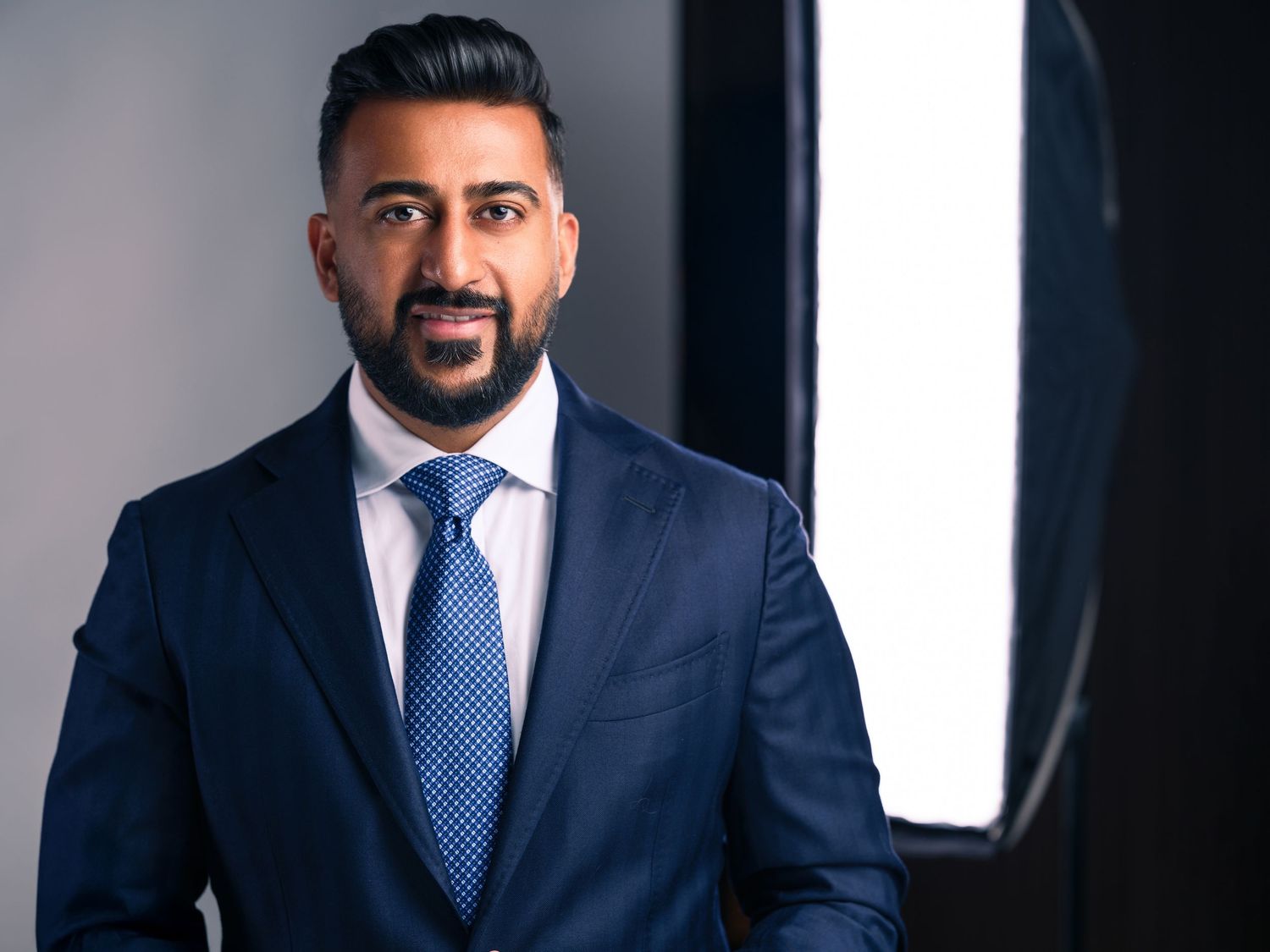 Professional business portraits featuring navy suit and blue tie against modern backdrop.