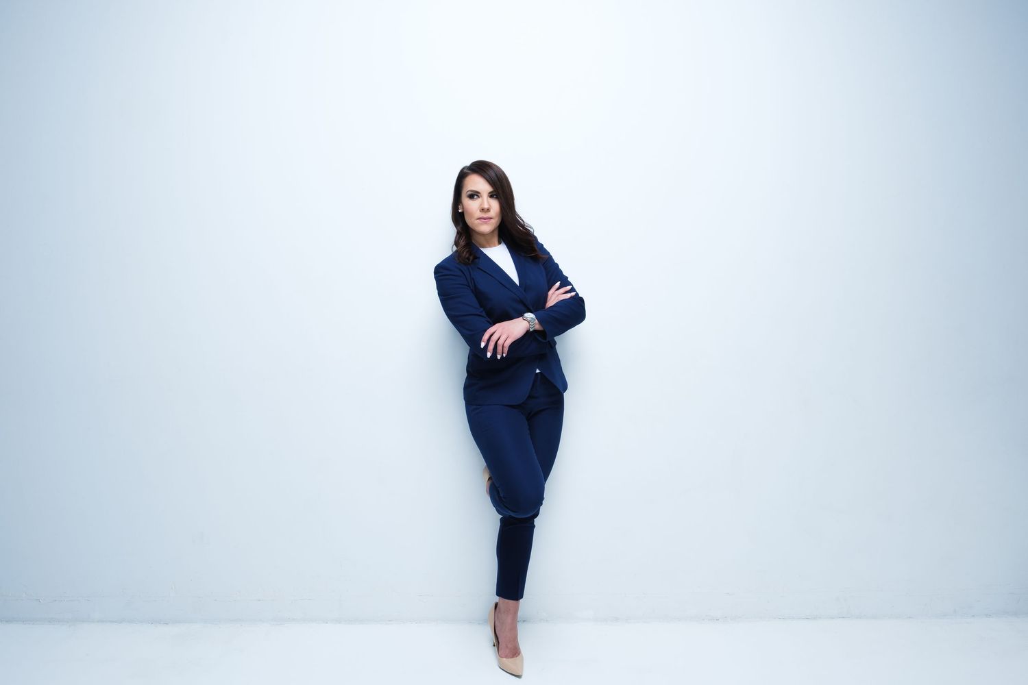 Woman in navy business attire poses against white background.