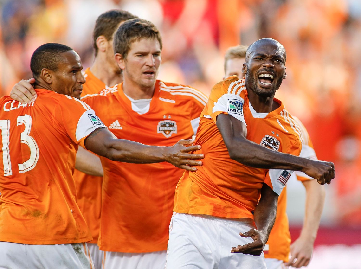 Soccer team in orange jerseys celebrates together on the field.