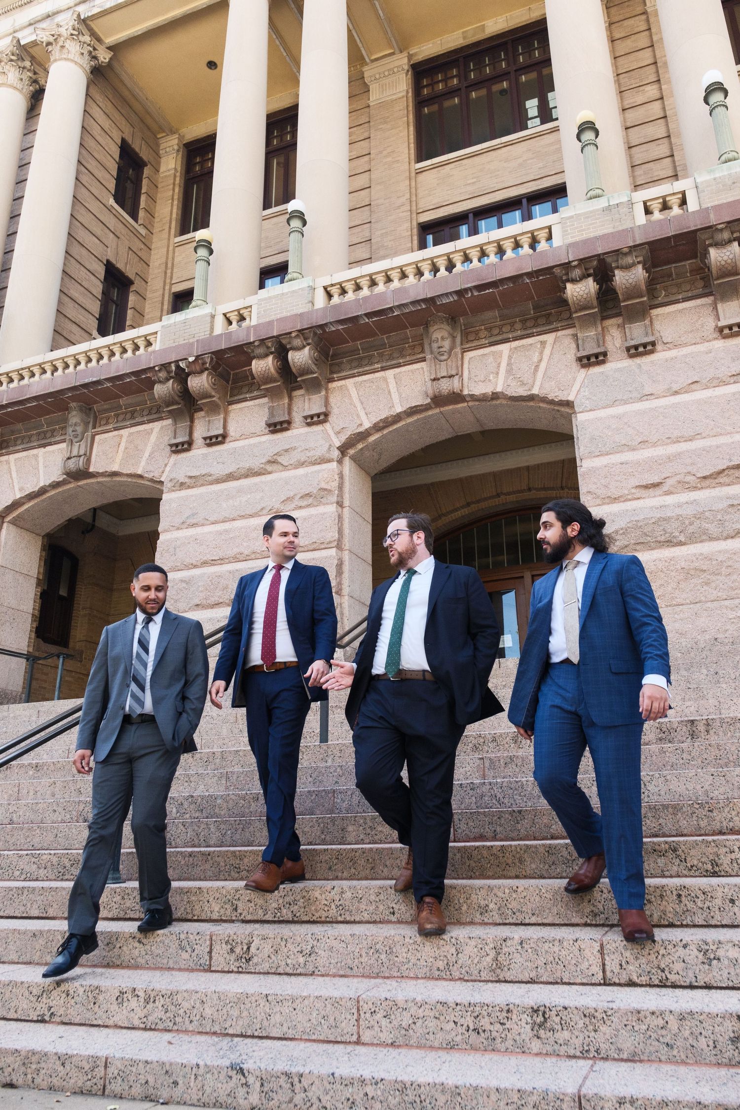 Group of lawyers in suits walking down courthouse steps with classical architecture.