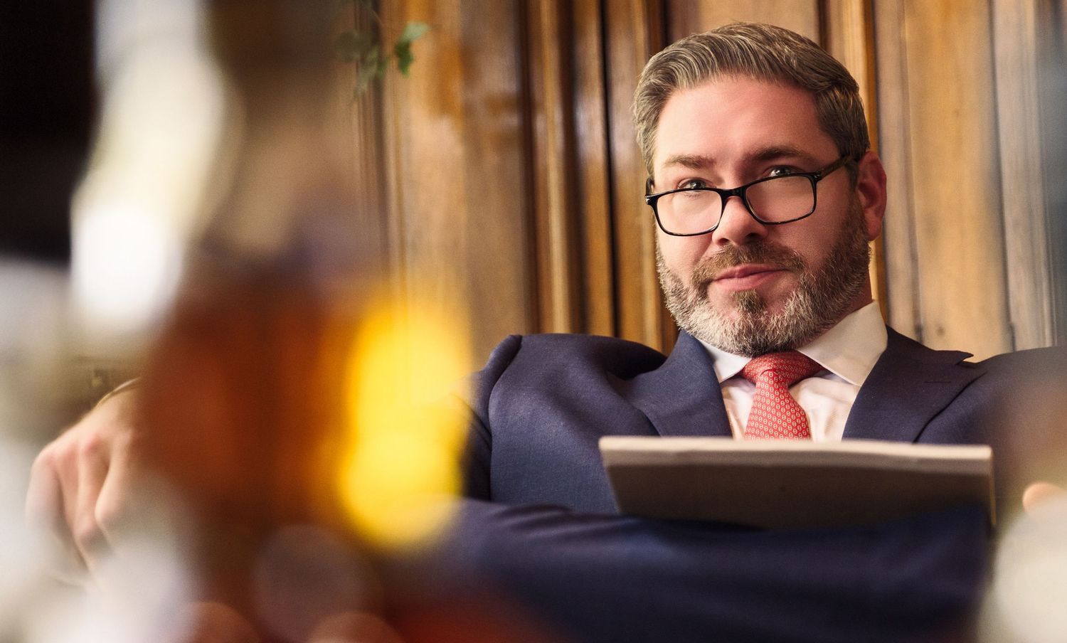 Professional in glasses reviewing documents in warm-lit office setting.