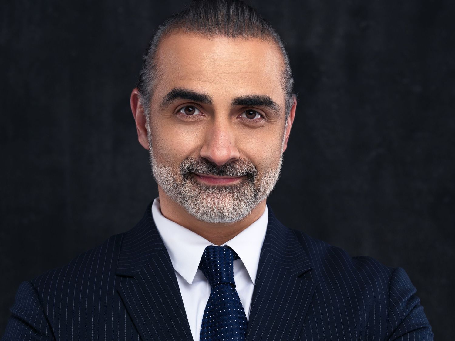 Professional portraits of someone in pinstripe suit and tie against dark background.