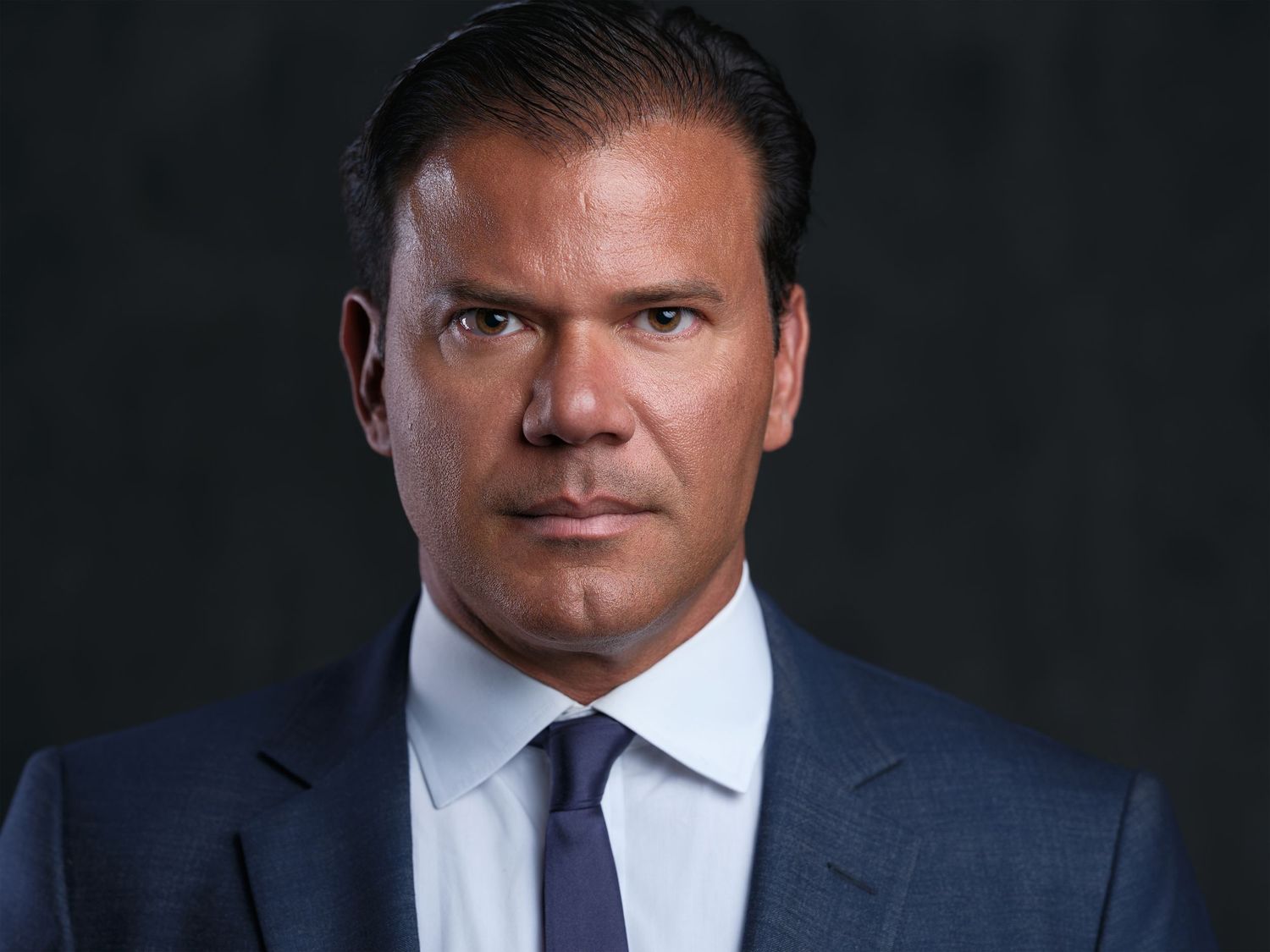 Executive style portrait of man in navy suit and tie against dark background.