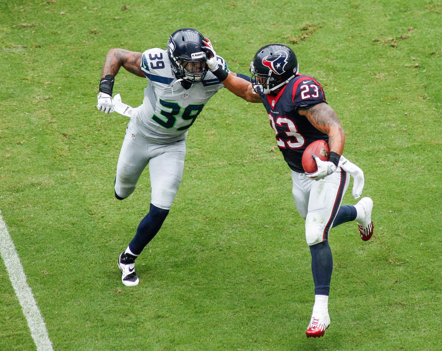 Football players dive and tackle on the grass field during game action.