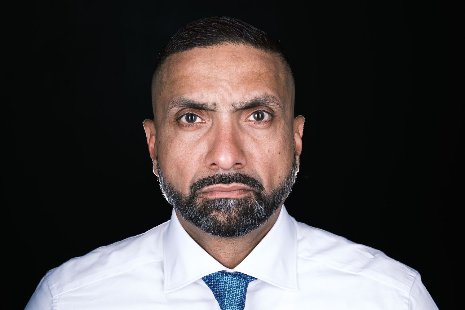 Professional headshot against black background wearing white shirt and blue tie.