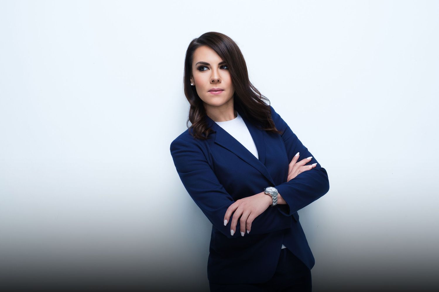Professional woman in navy blazer with arms crossed against light background.
