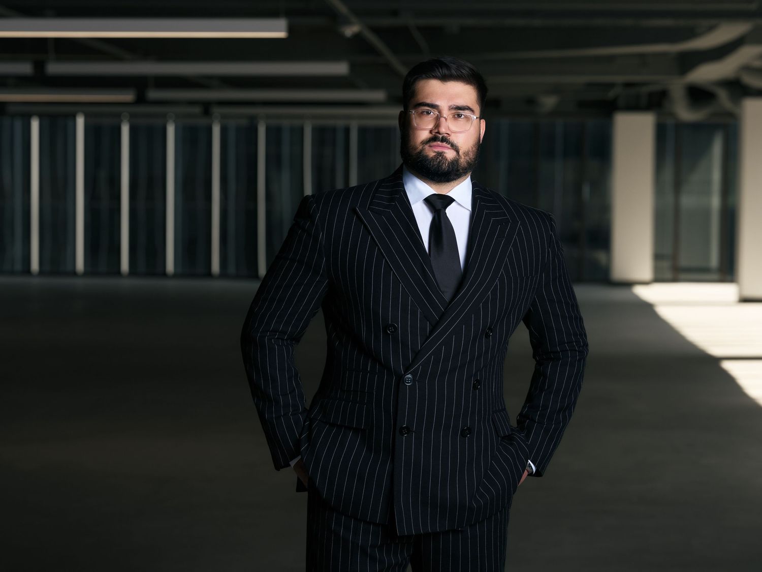 Professional in a pinstriped double-breasted suit stands confidently in a dimly lit industrial space.