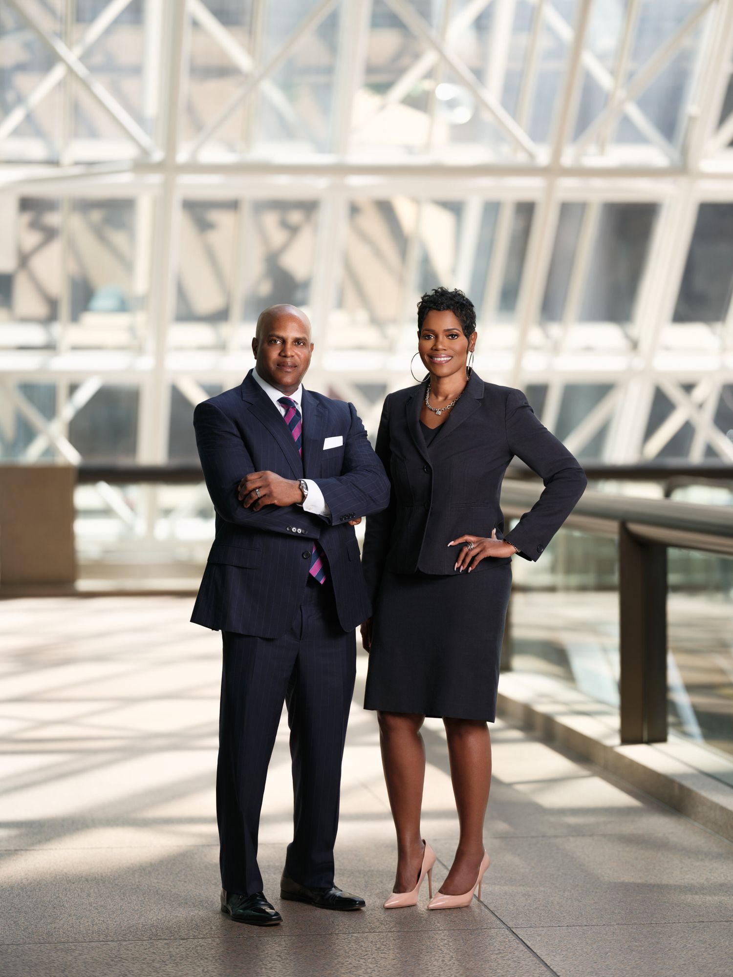 Two professionals in business attire standing in modern office building with architectural features.
