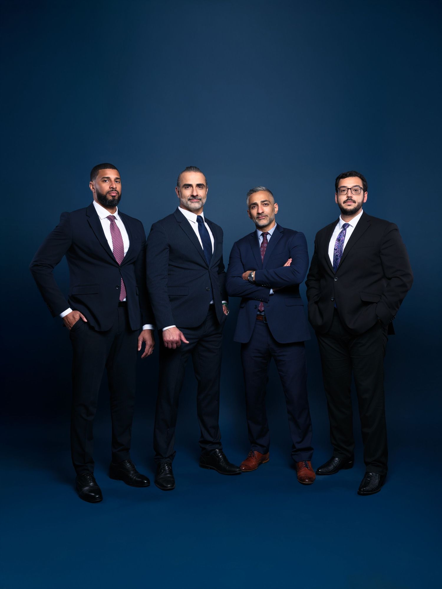 Four business professionals in dark suits standing against deep blue background.