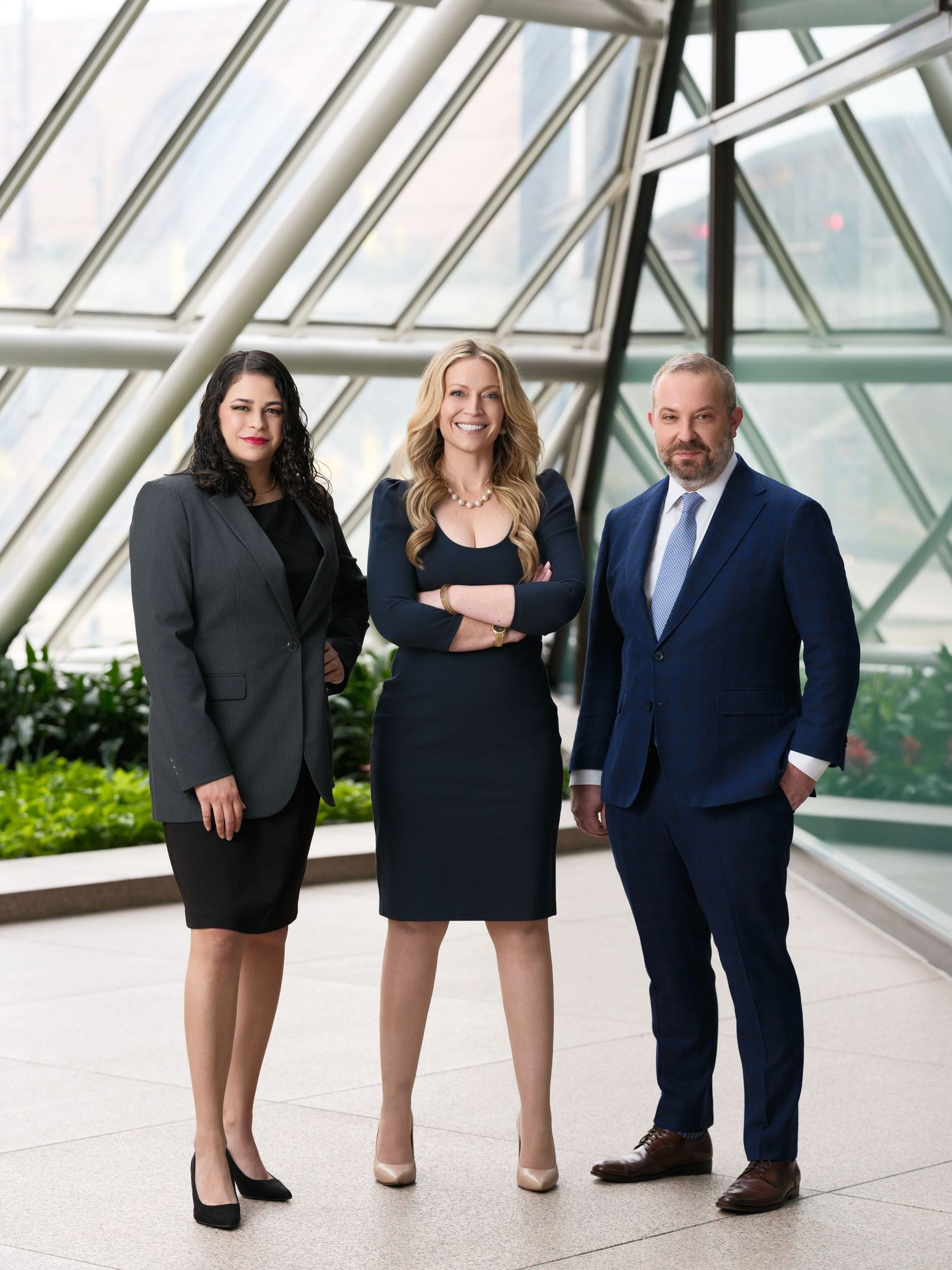 Three business professionals standing in modern glass atrium with natural lighting.