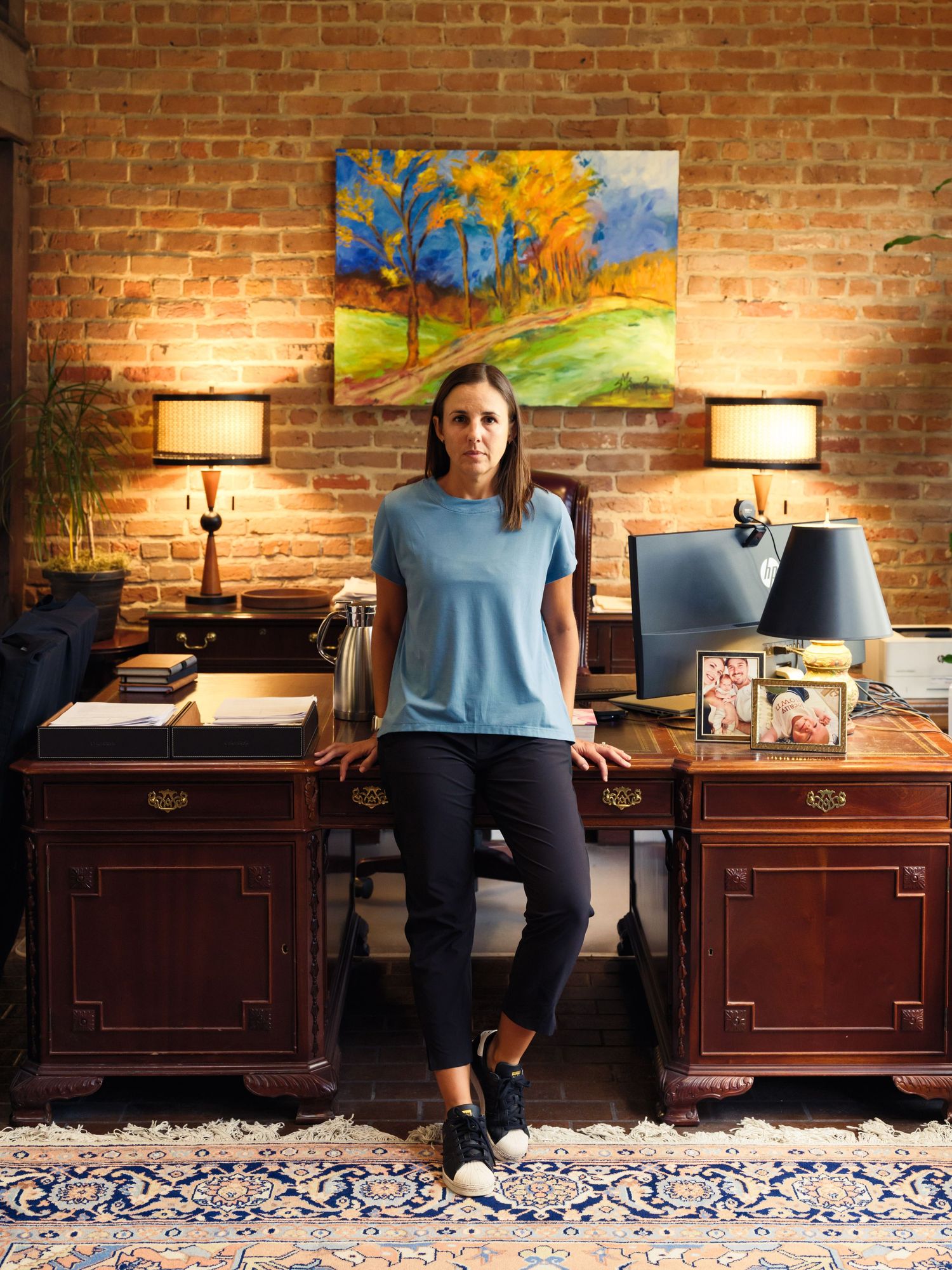 Professional seated between two wooden desks with colorful artwork on exposed brick wall.
