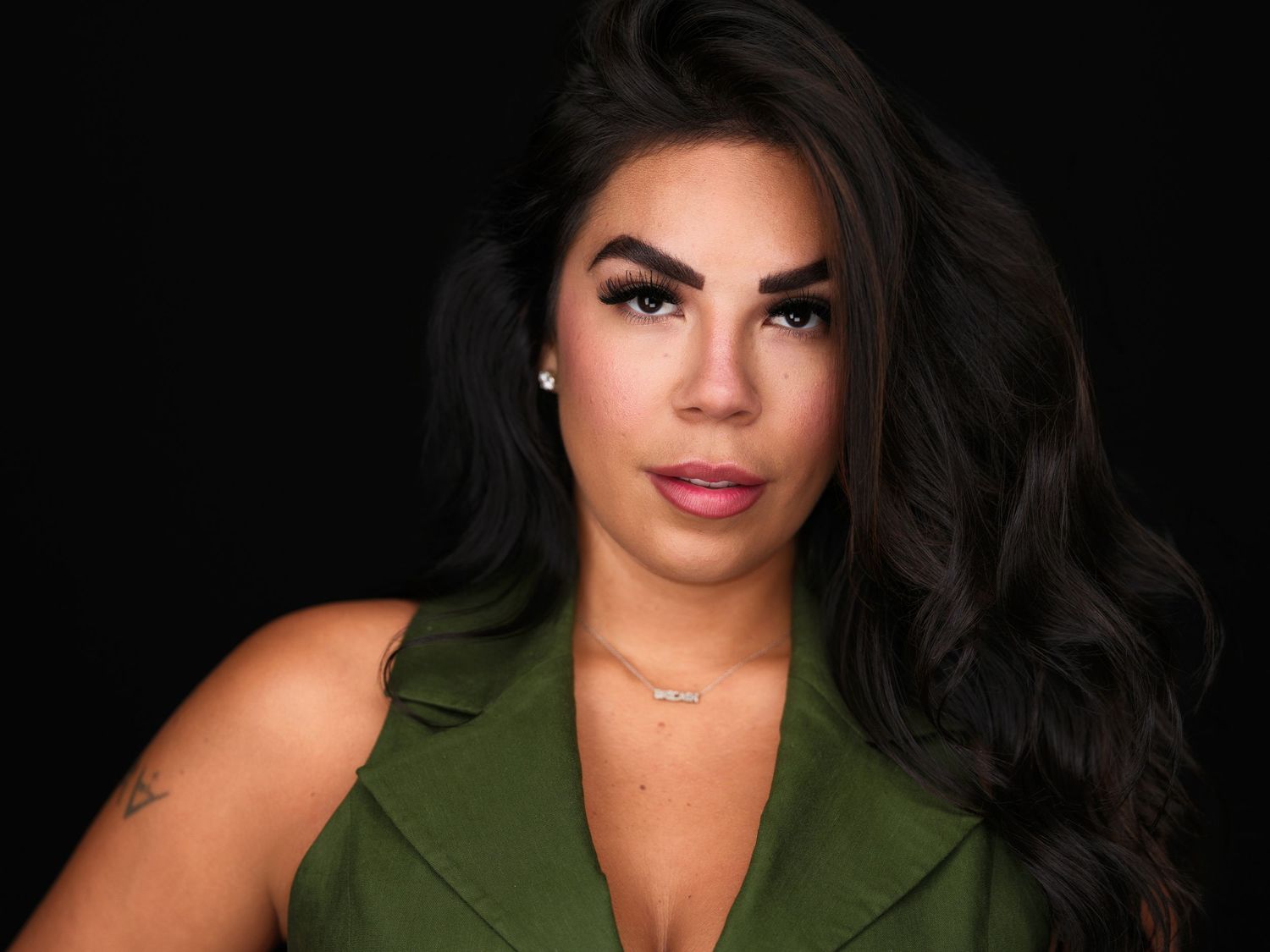 Woman with long dark hair wearing a green top poses against a dark background in a professional portrait photo.