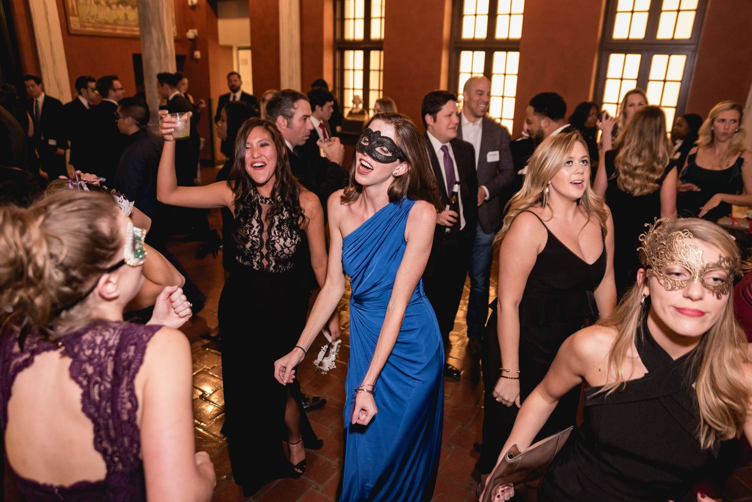 Group of formally dressed people dancing and celebrating at an elegant indoor venue.