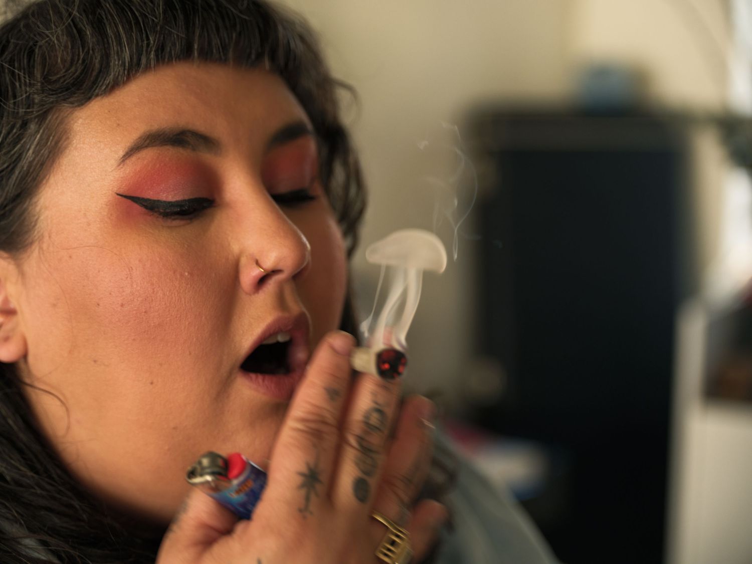 Person with red eyeshadow exhaling smoke in dramatic lighting.