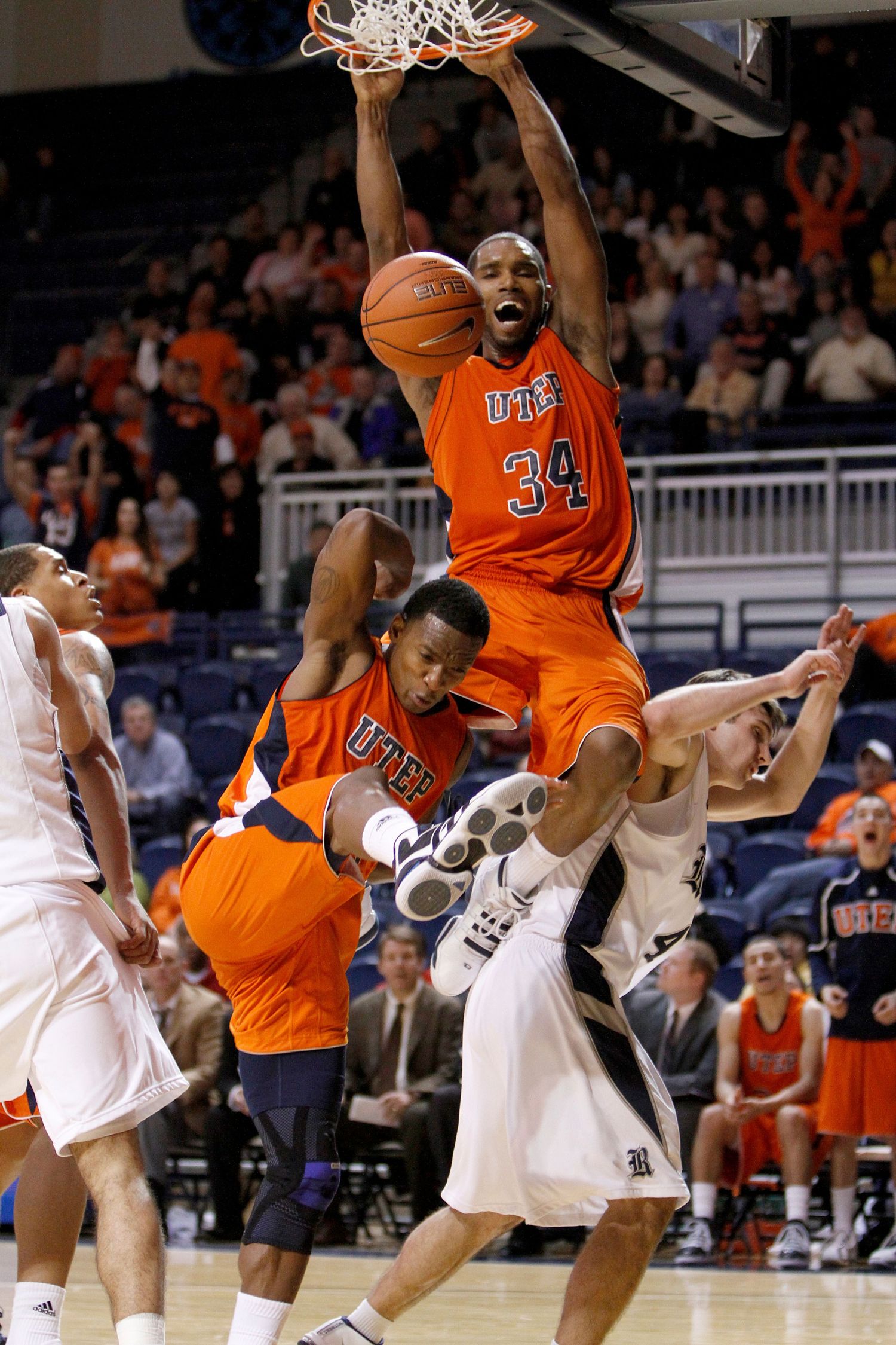 Basketball player in orange uniform performs powerful slam dunk during intense game action.