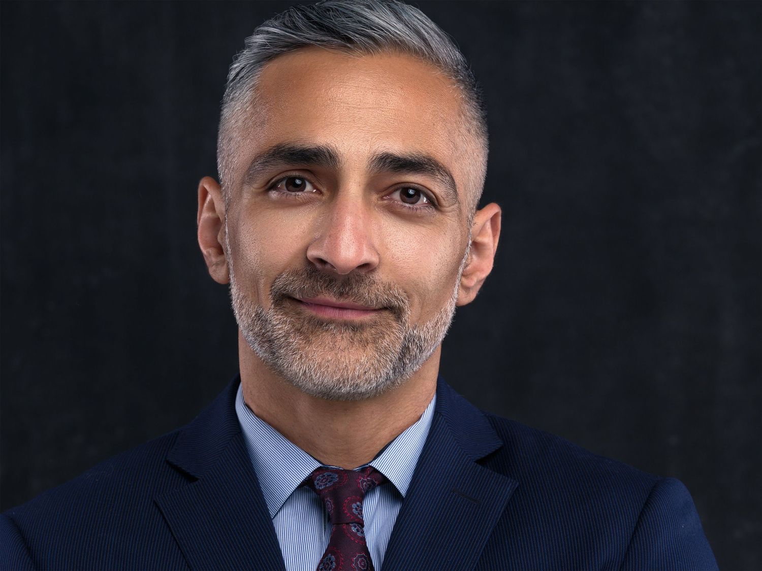Professional headshot series showing someone in a navy suit jacket with varying expressions against a dark background.