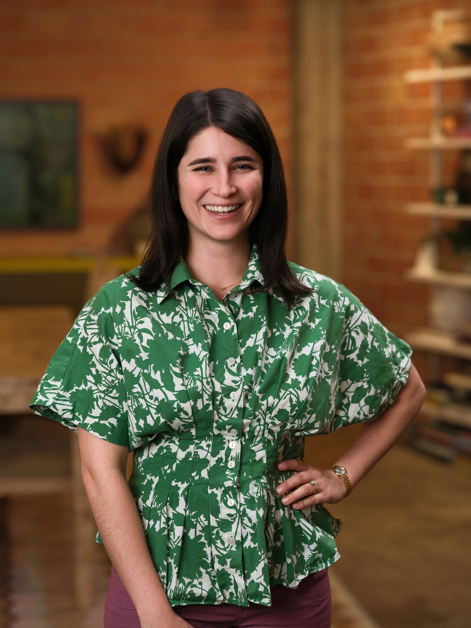 Person wearing a green floral print blouse poses against brick wall background.