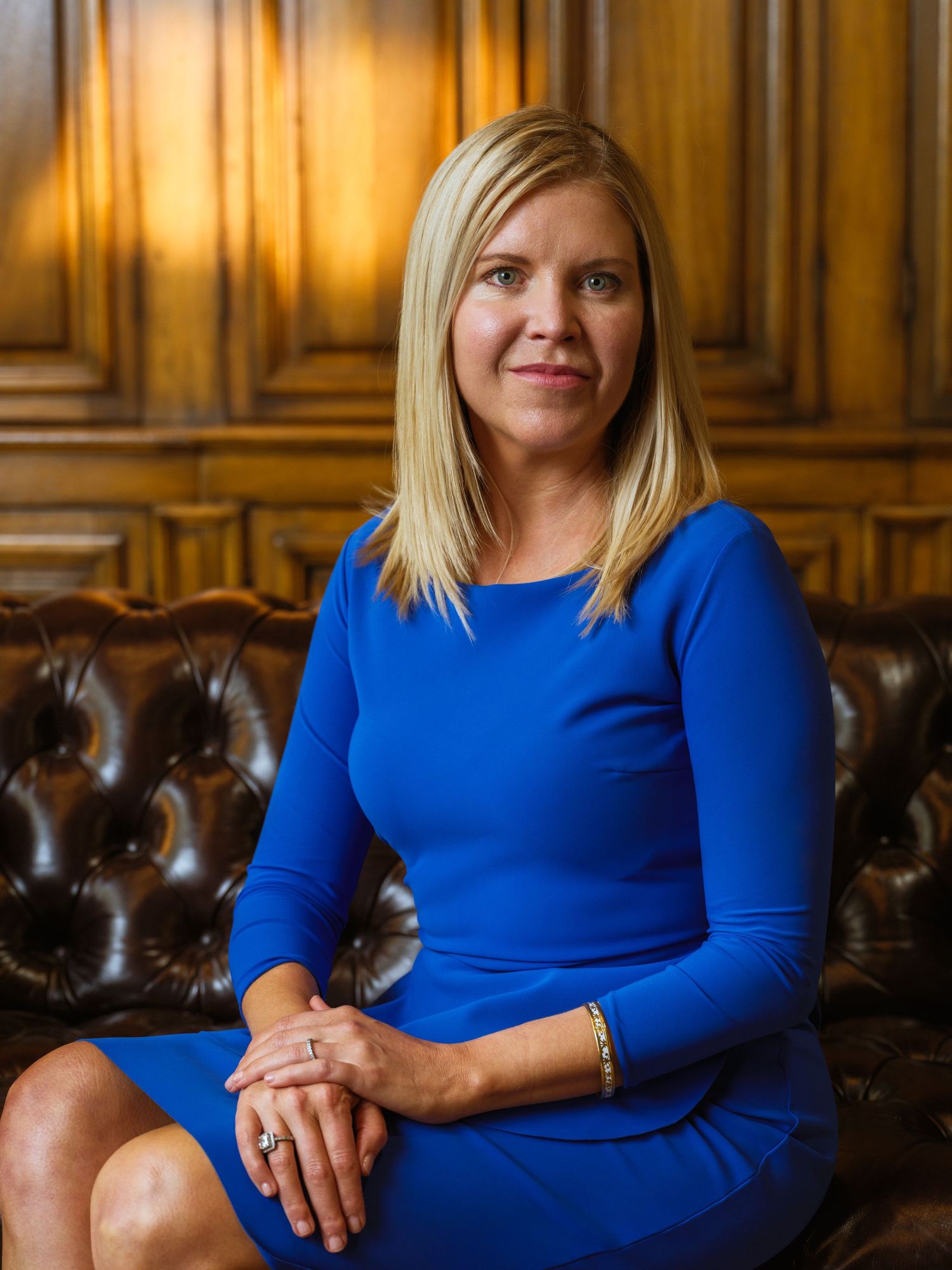 Portrait of professional in fitted blue dress seated on vintage leather couch.