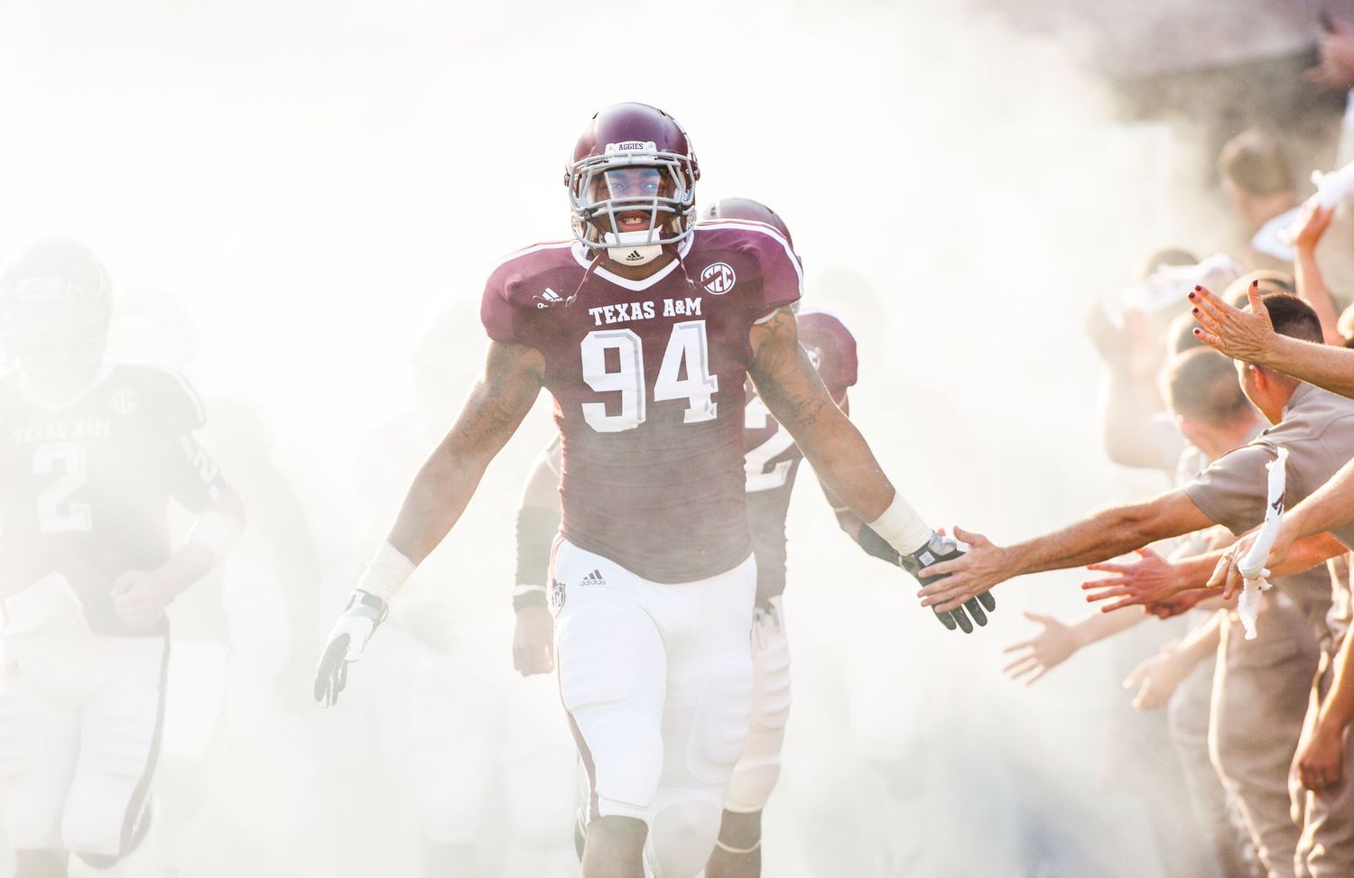 Football player emerges through smoke effects during team entrance at stadium.