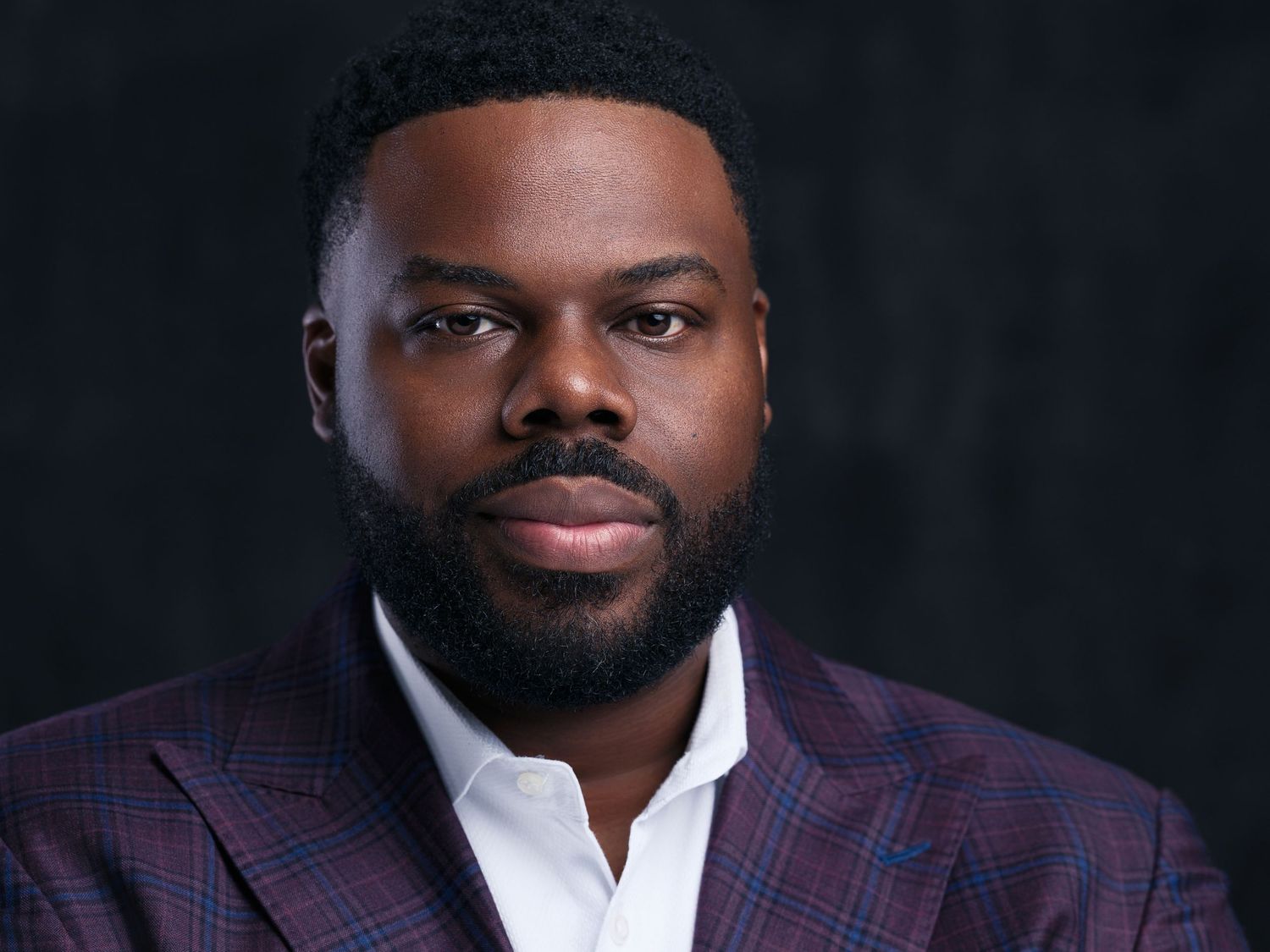 Professional headshot of someone wearing a dark suit against a black background.