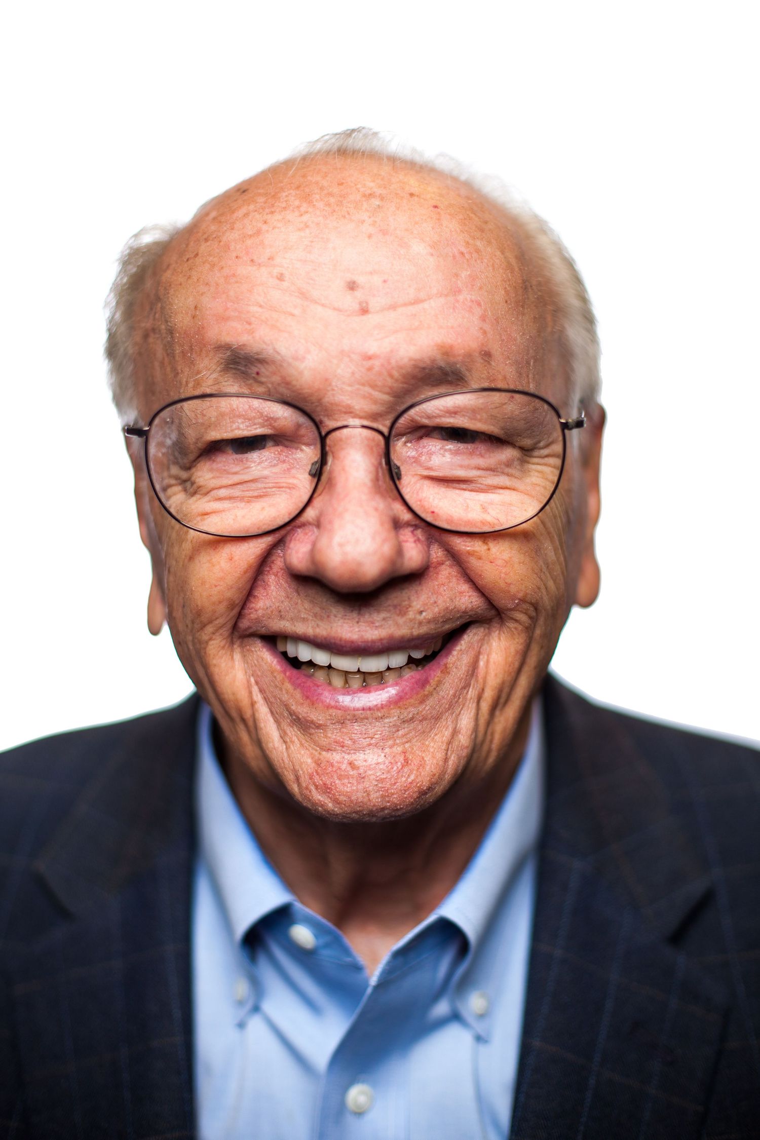 Portrait of an elderly person wearing glasses and a blue shirt smiling warmly at the camera.