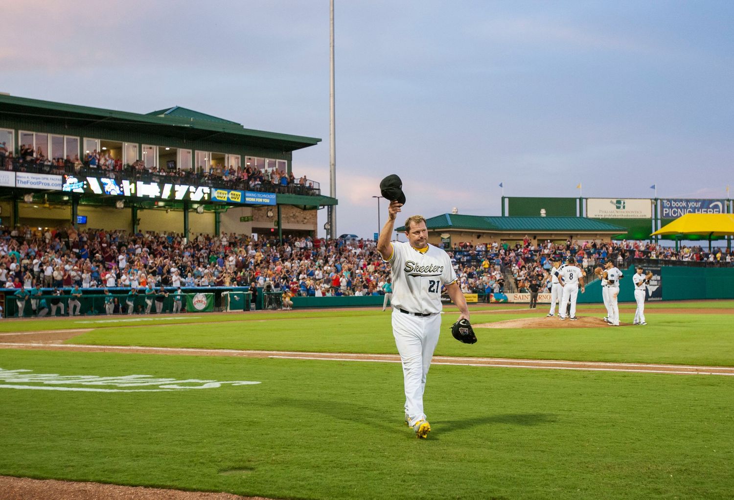 Baseball player acknowledges crowd in minor league stadium during daytime game.