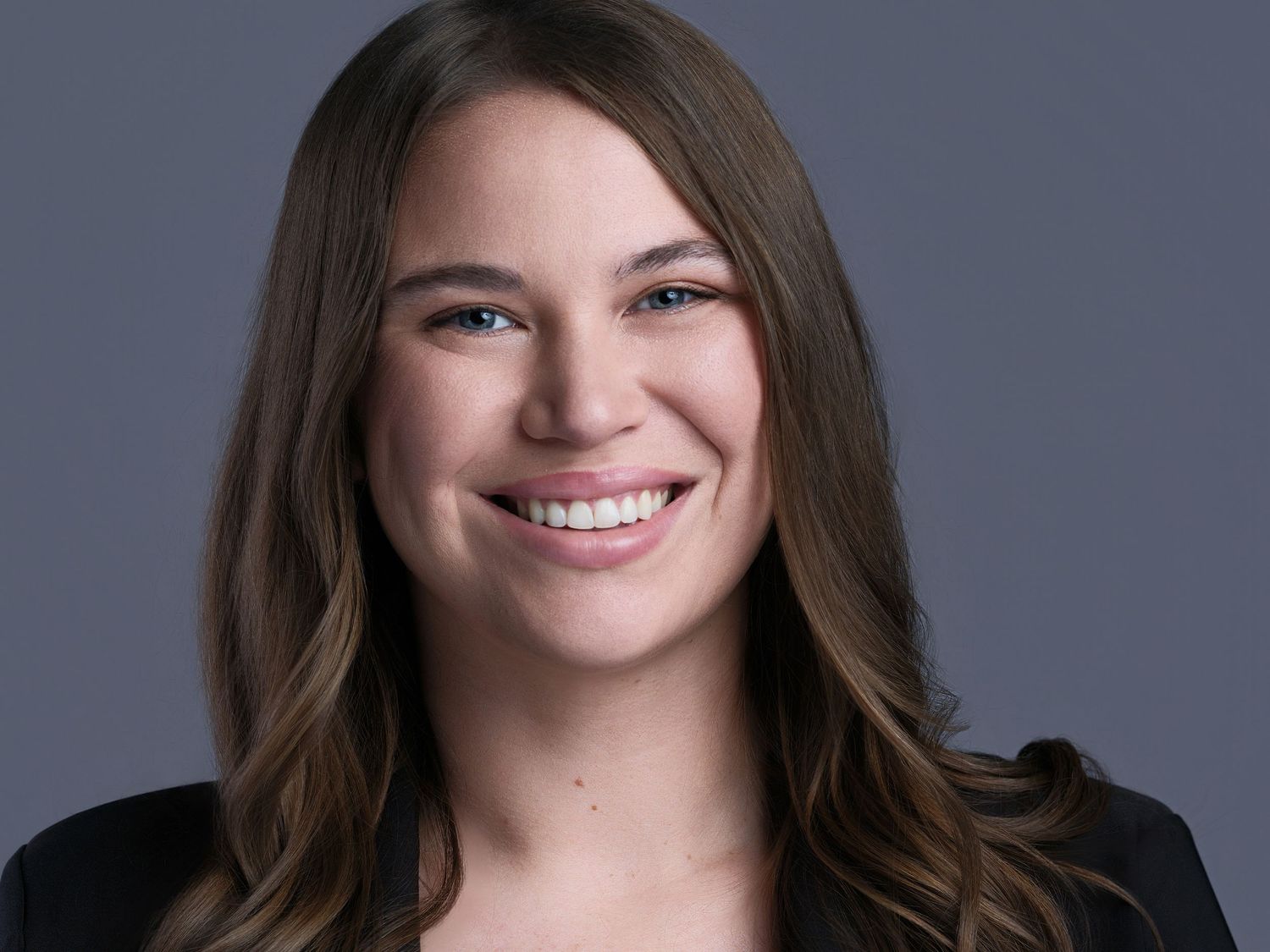 Professional headshot against grey backdrop showing warm smile.