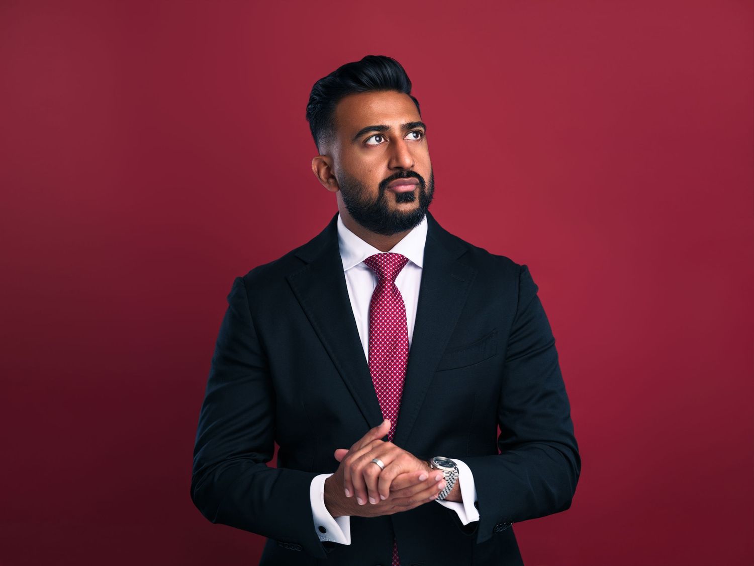 Professional portrait of person in dark suit and red tie against burgundy background.