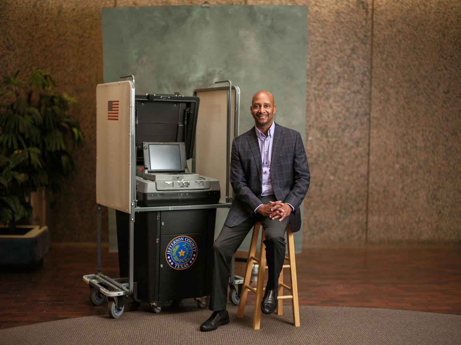 Person in business attire sitting on stool next to office equipment in corporate setting.