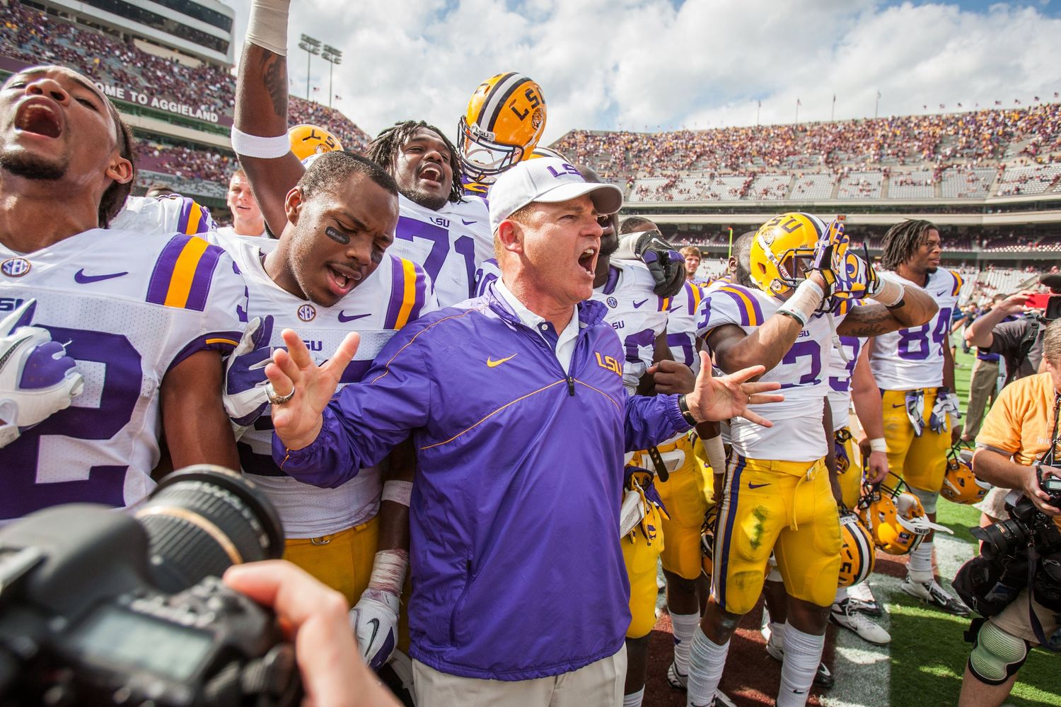 Football fans and players celebrate together in a packed college stadium.