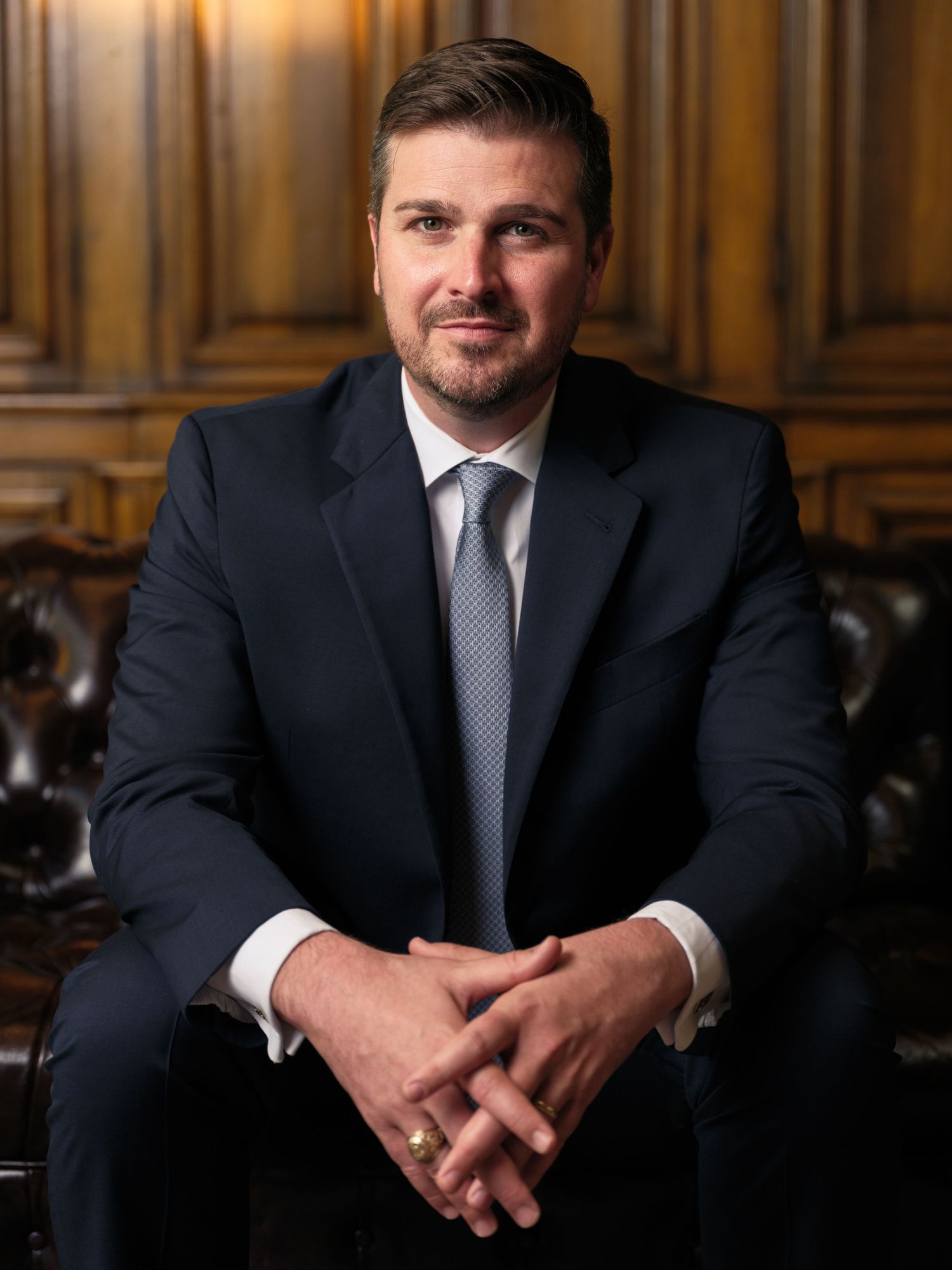 Professional in dark suit and tie seated on leather sofa in elegant office setting.