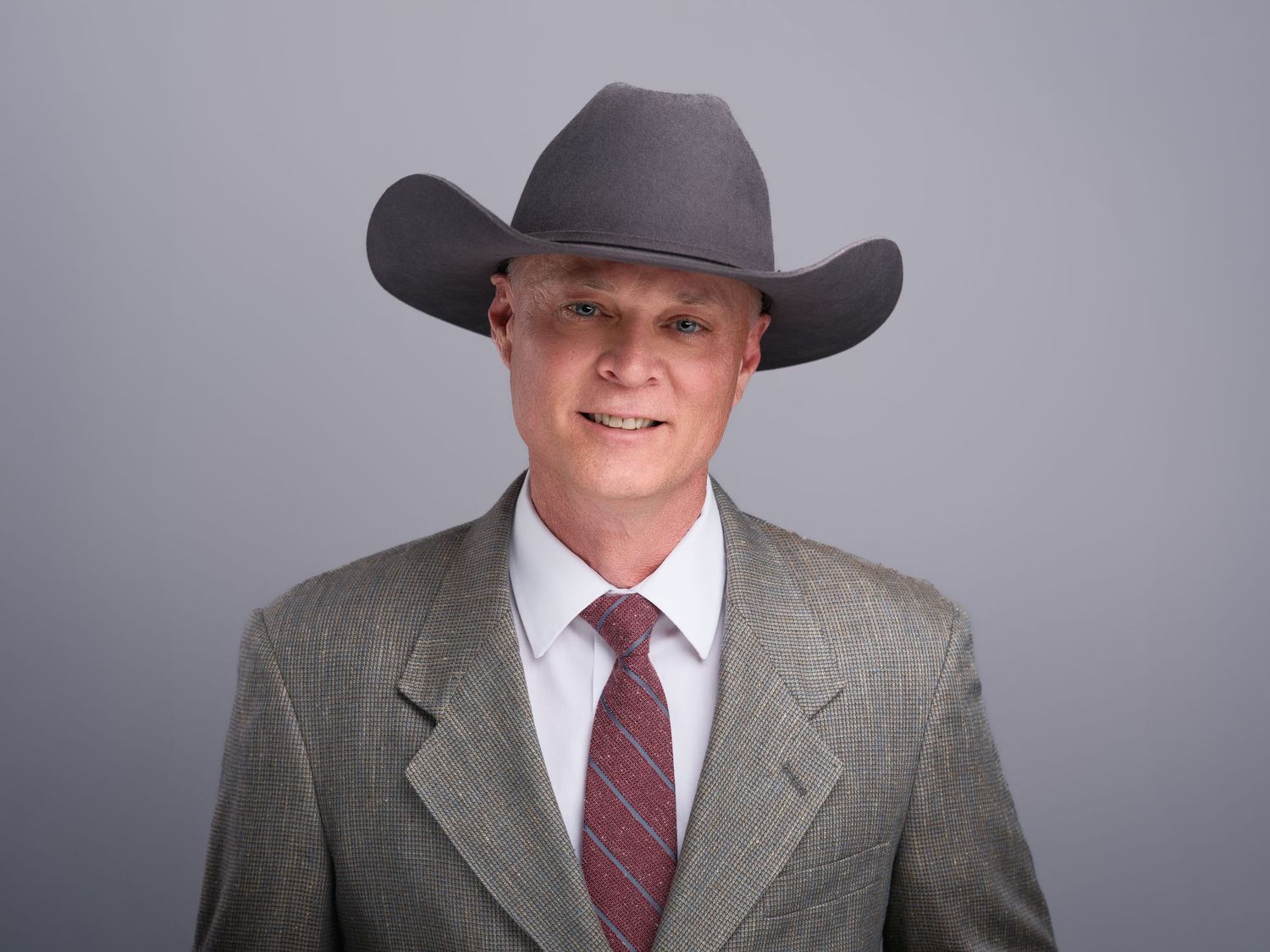 Business portrait of a person wearing a cowboy hat and gray suit with burgundy tie.