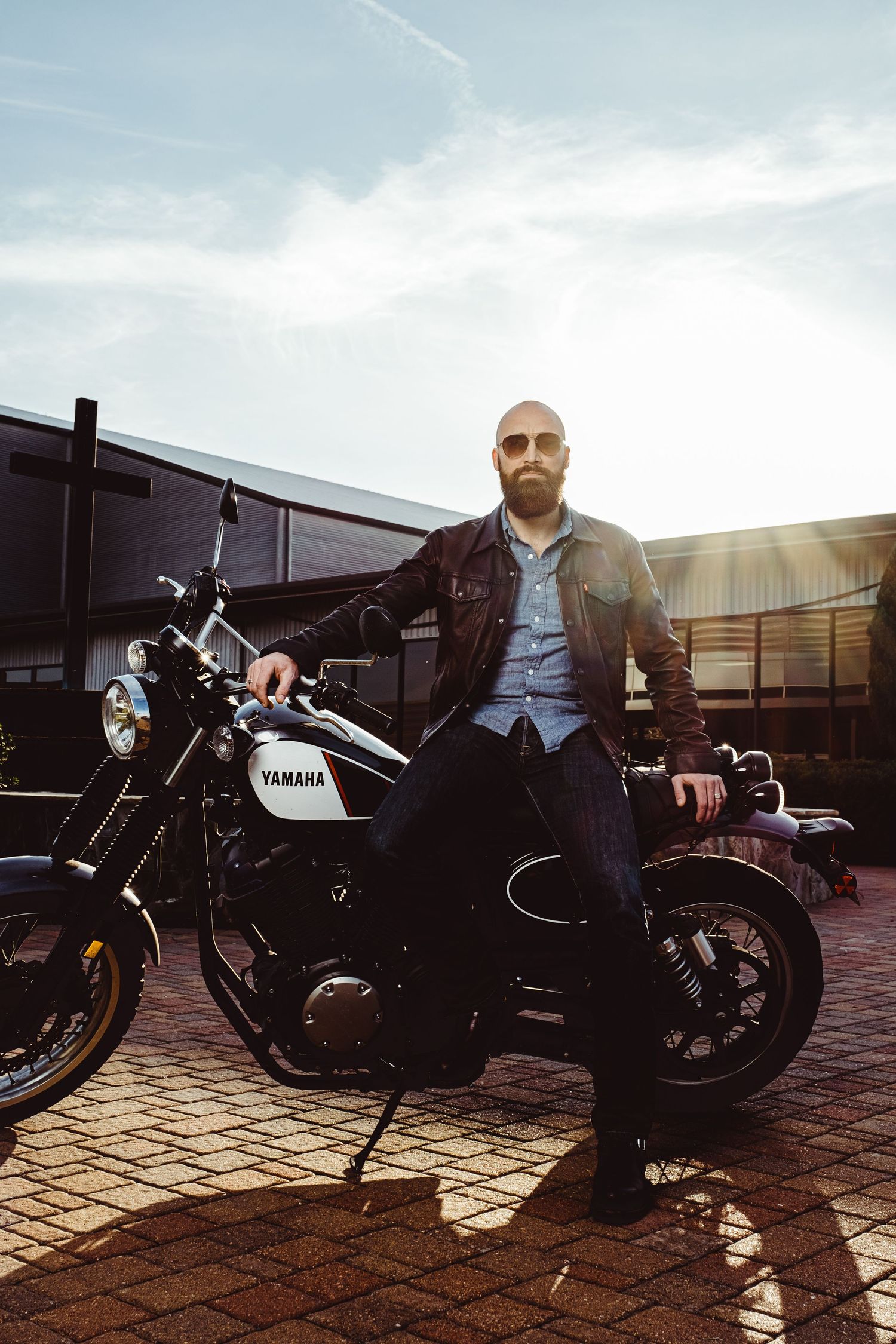 Person in a leather jacket sitting on a black Yamaha motorcycle at sunset.