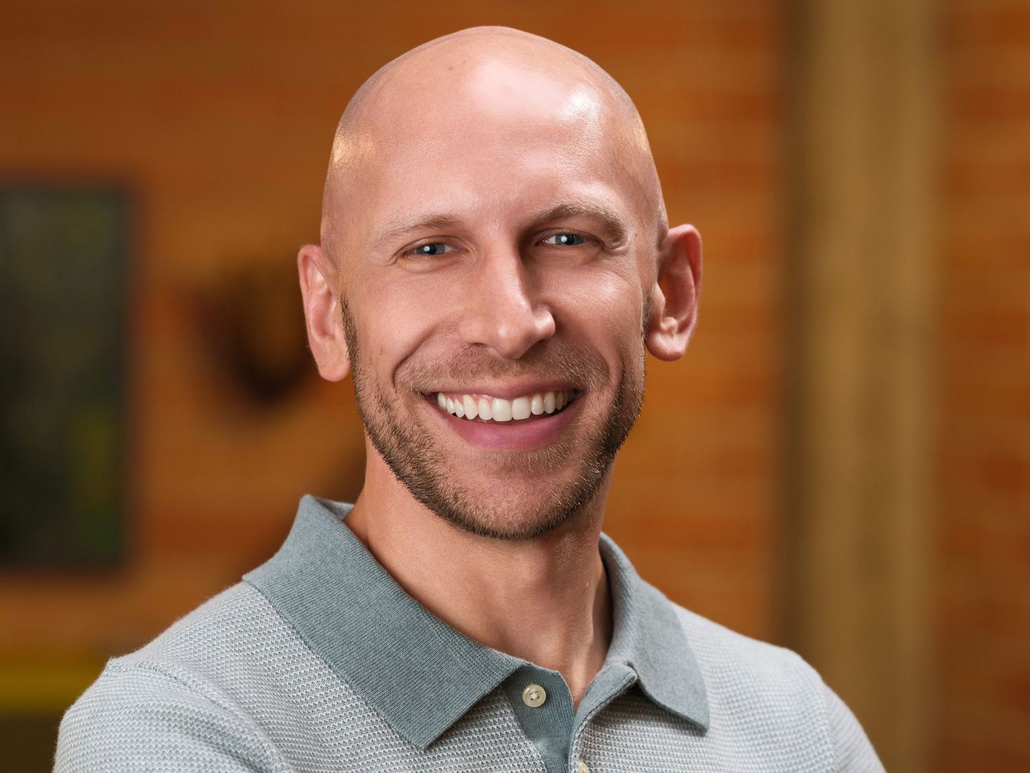Professional headshot against warm brick background with natural lighting.