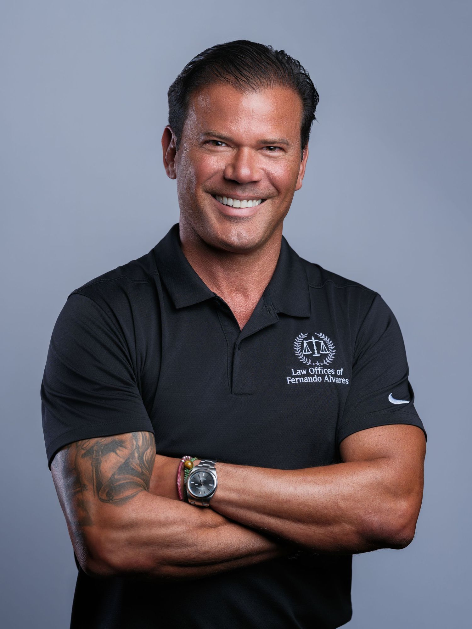 Confident man in black polo shirt with muscular arms crossed wearing large watch.