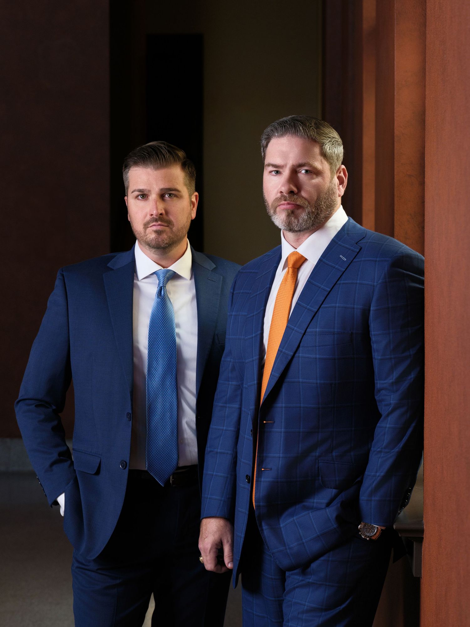 Two businessmen in navy suits standing together in professional corporate portrait.