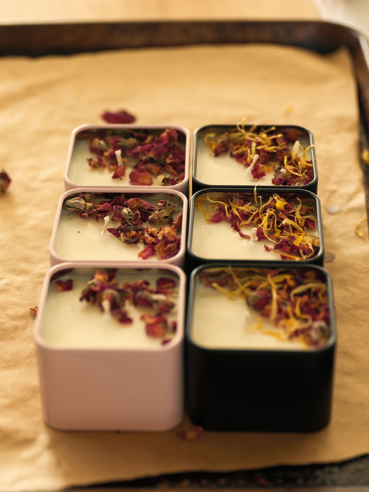 Six metal tins containing dried flower petals arranged in rows on beige fabric.