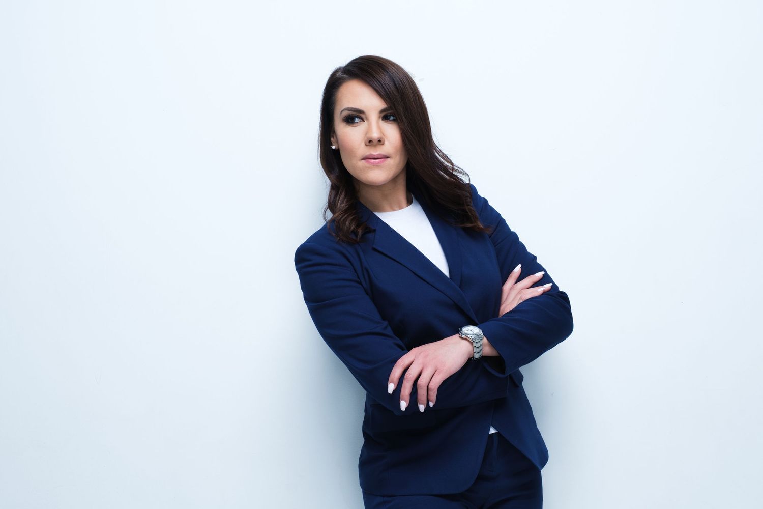 Professional portrait of a businesswoman in navy suit with arms crossed against white background.