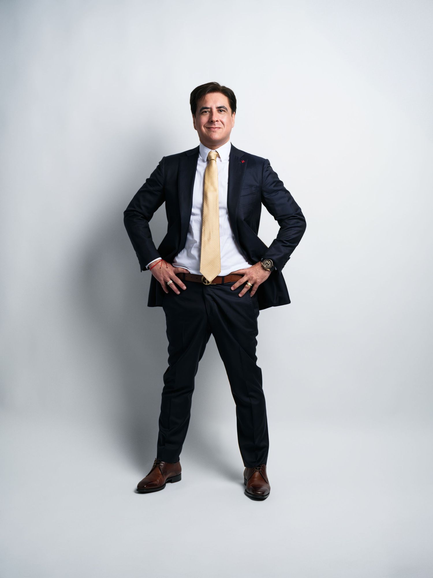 Professional full-length studio portrait in dark suit with yellow tie against white background.