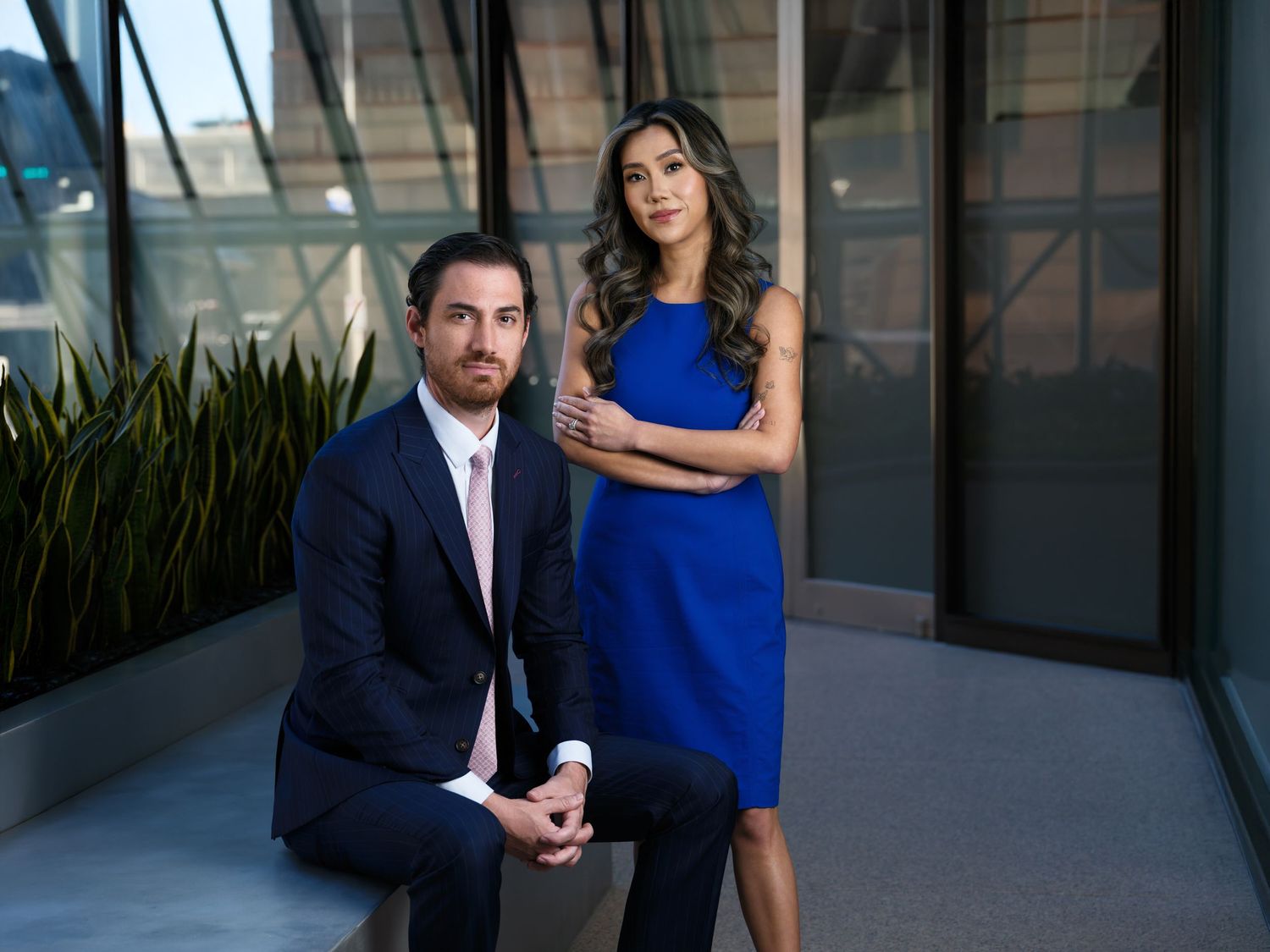 Professional business portrait of two colleagues in formal attire posing on modern office balcony.