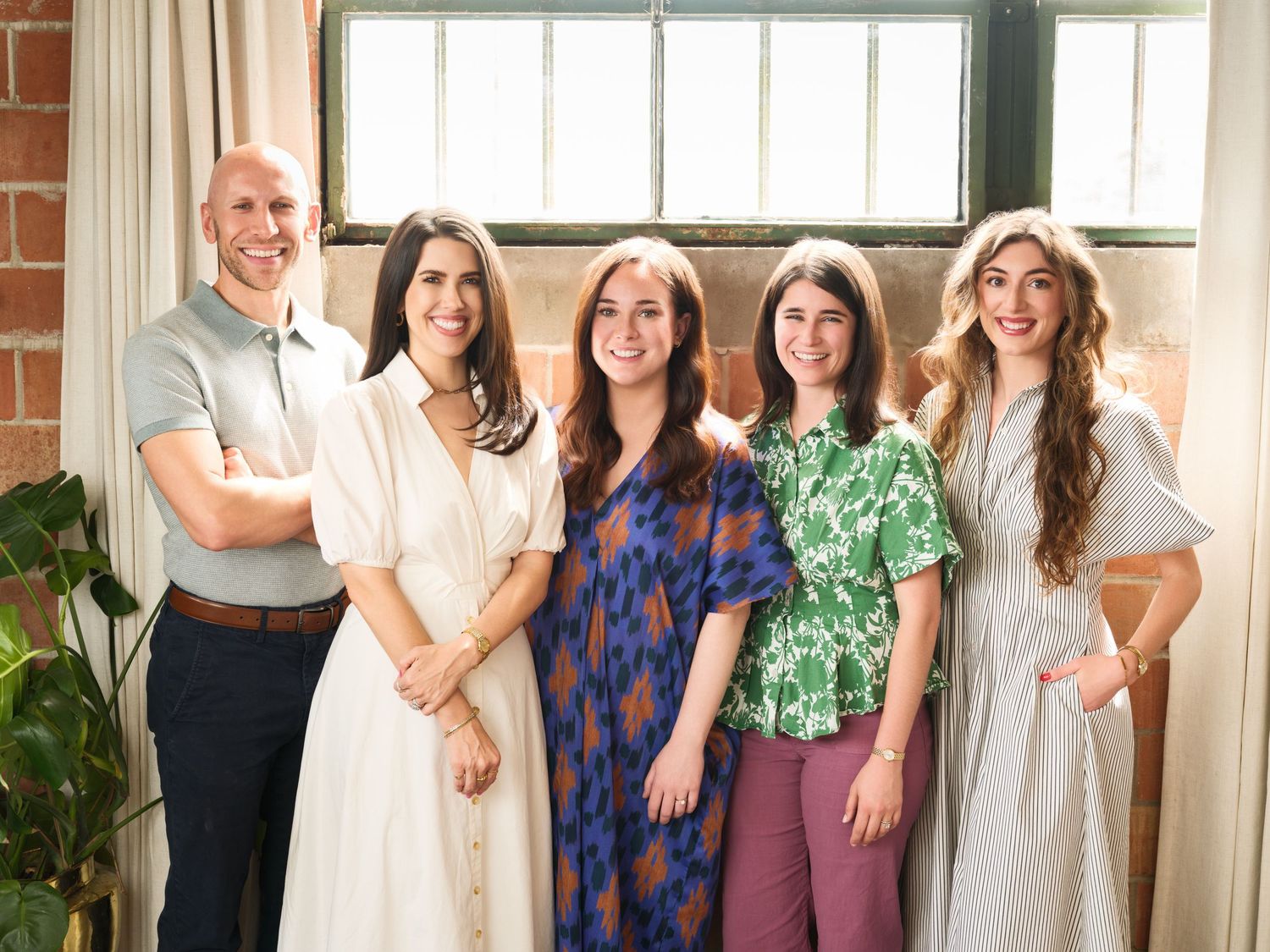 Group photo of five colleagues in casual business attire standing together in a bright office space.
