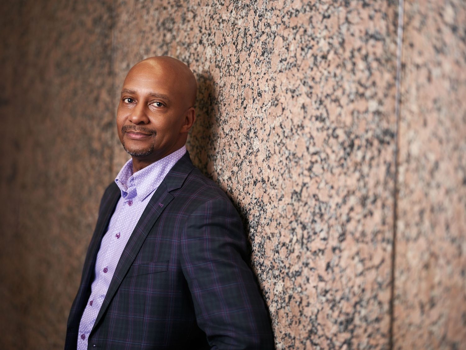 Professional business portrait of a person in plaid suit against textured marble wall.