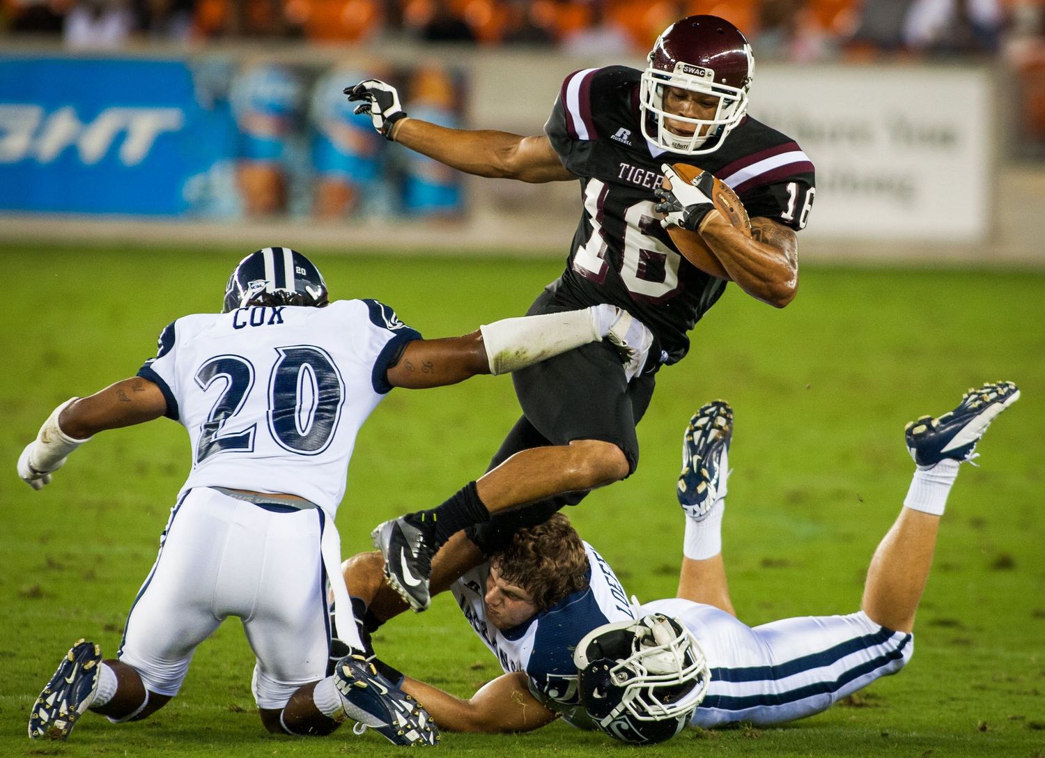 Football player leaps over defenders during dramatic college football play.