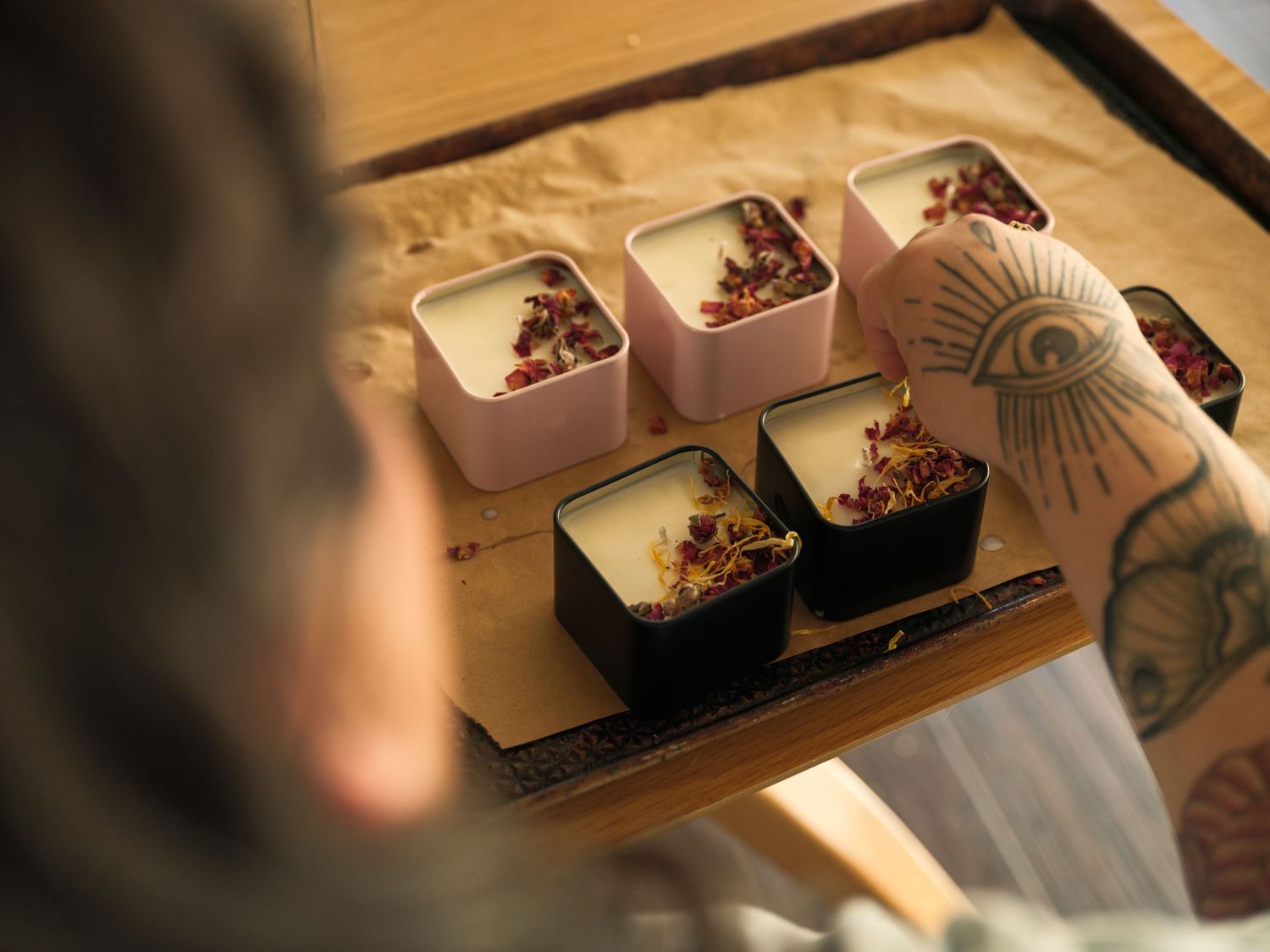 Chef preparing elegant desserts in pink and black serving dishes on a wooden surface.
