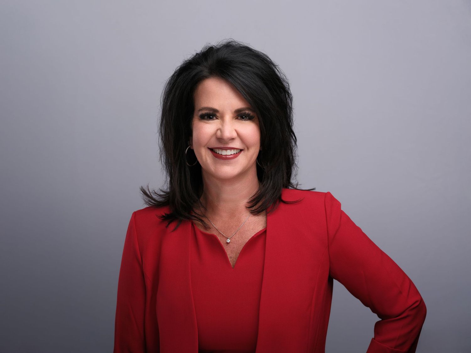 Professional portrait featuring a bright red blazer against a gray studio background.