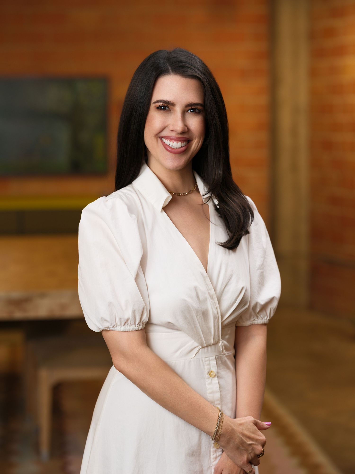 Professional portrait in white blouse against brick wall background.