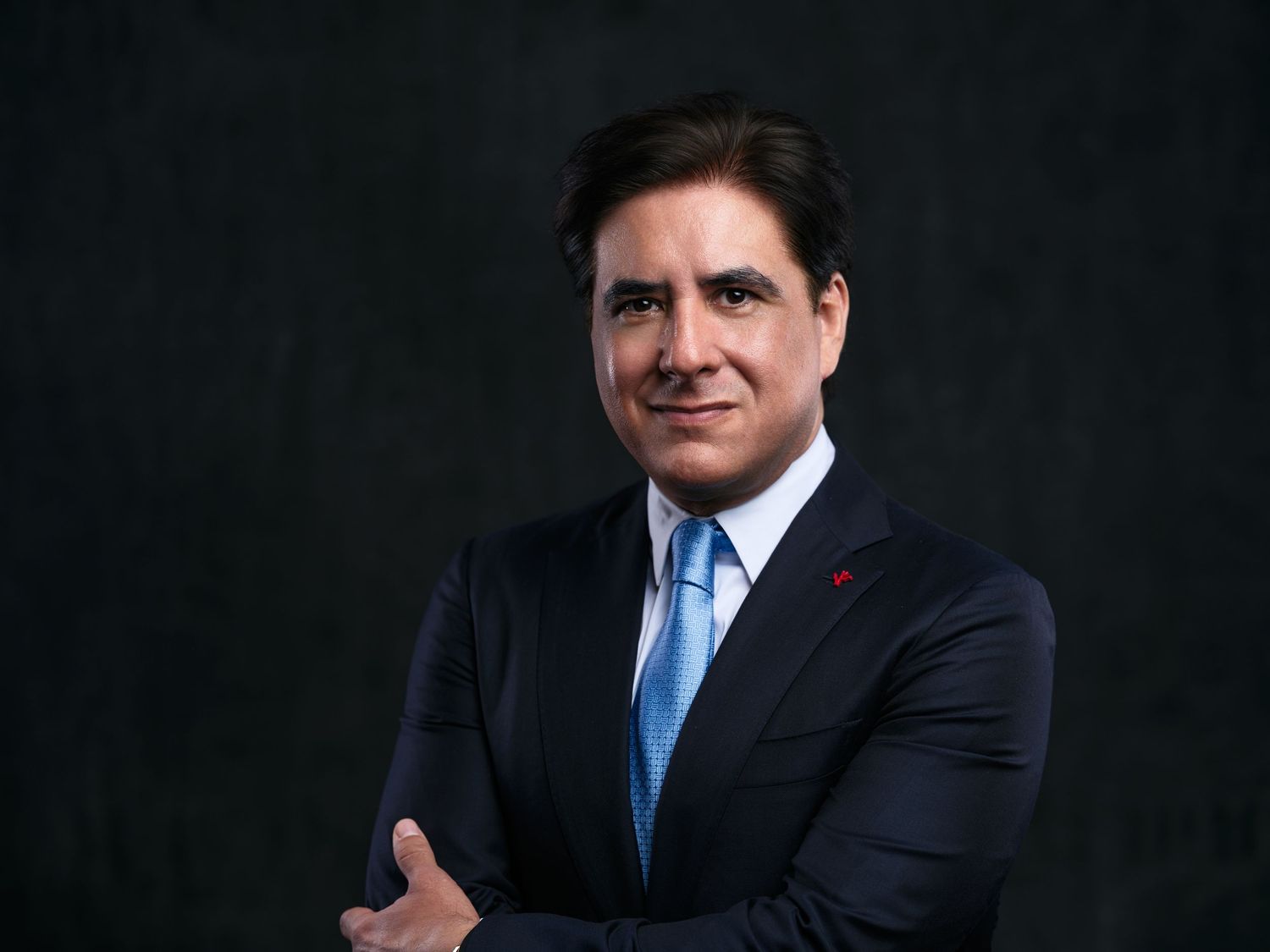 Business portrait in dark suit and light blue tie against dramatic black backdrop.