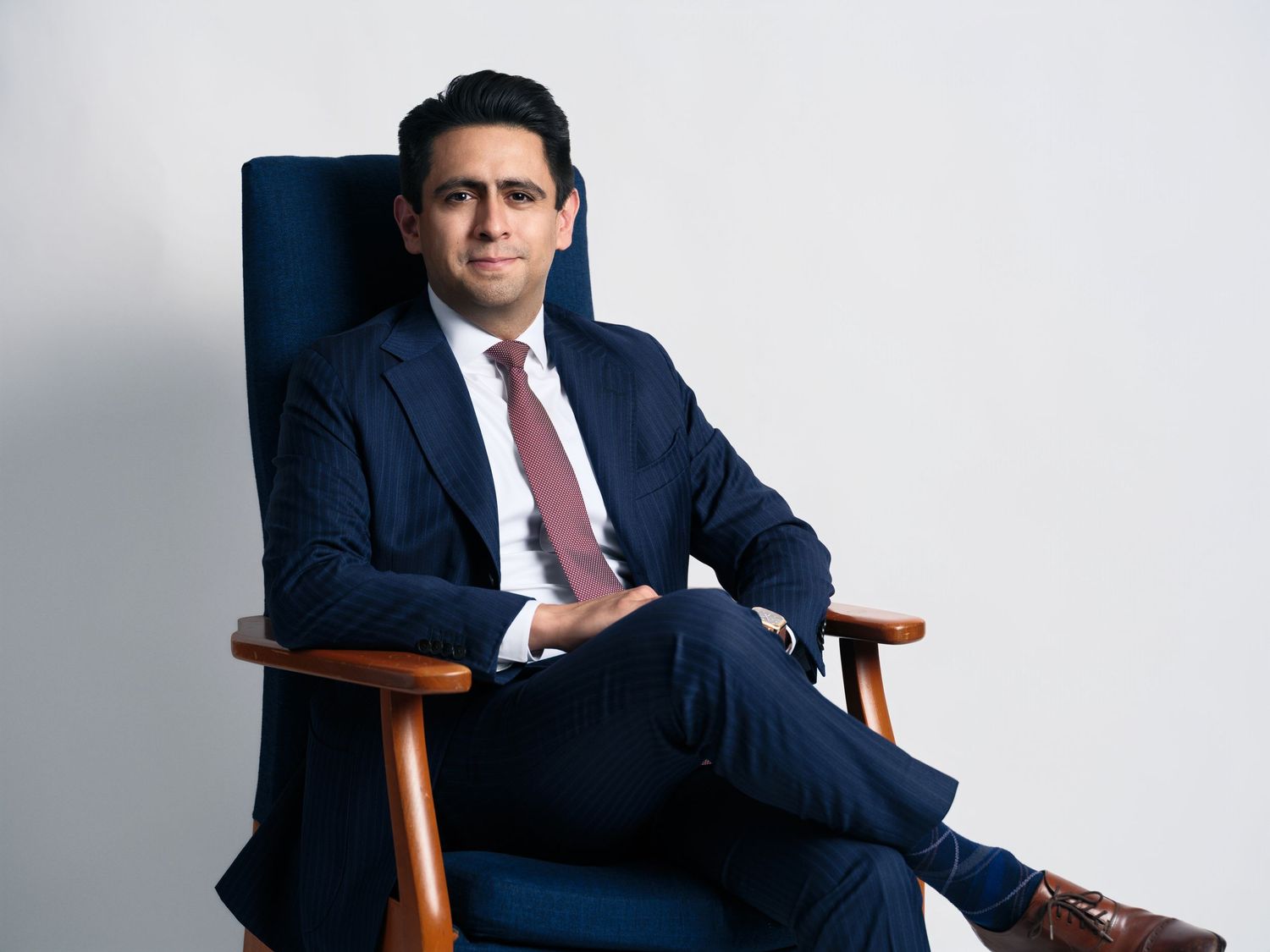 Executive in a dark business suit seated in a wooden chair against a white background.